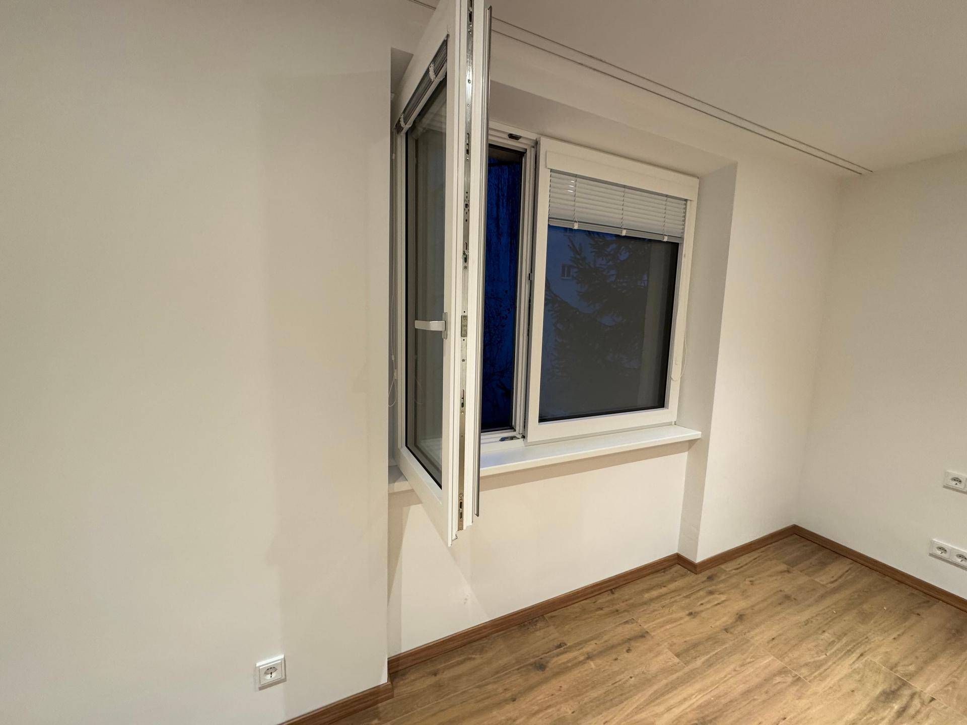 Geöffnetes Fenster mit Jalousien in einem hellen Raum.