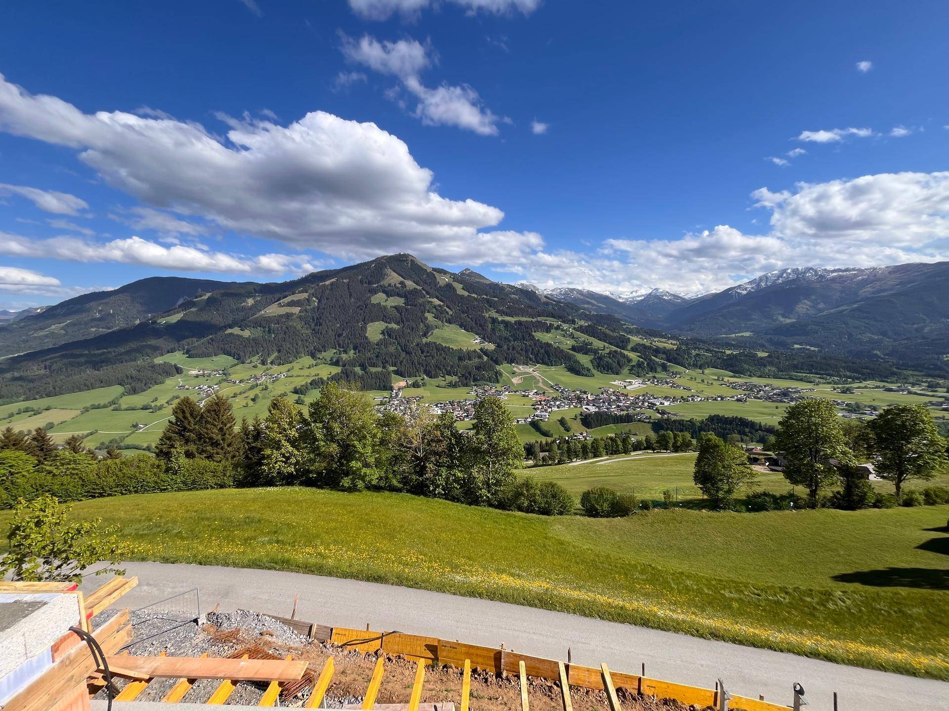 Weitläufiger Panoramablick über grüne Hügel und Täler mit majestätischen Bergen im Hintergrund unter blauem Himmel.