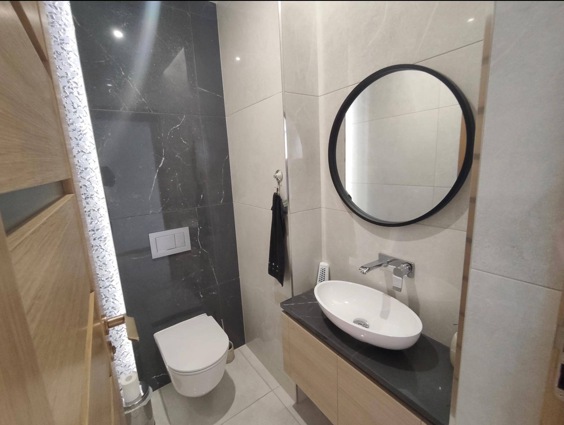 Modernes Gäste-WC mit Wand-WC, Einzelwaschbecken und dunklen Akzentfliesen.