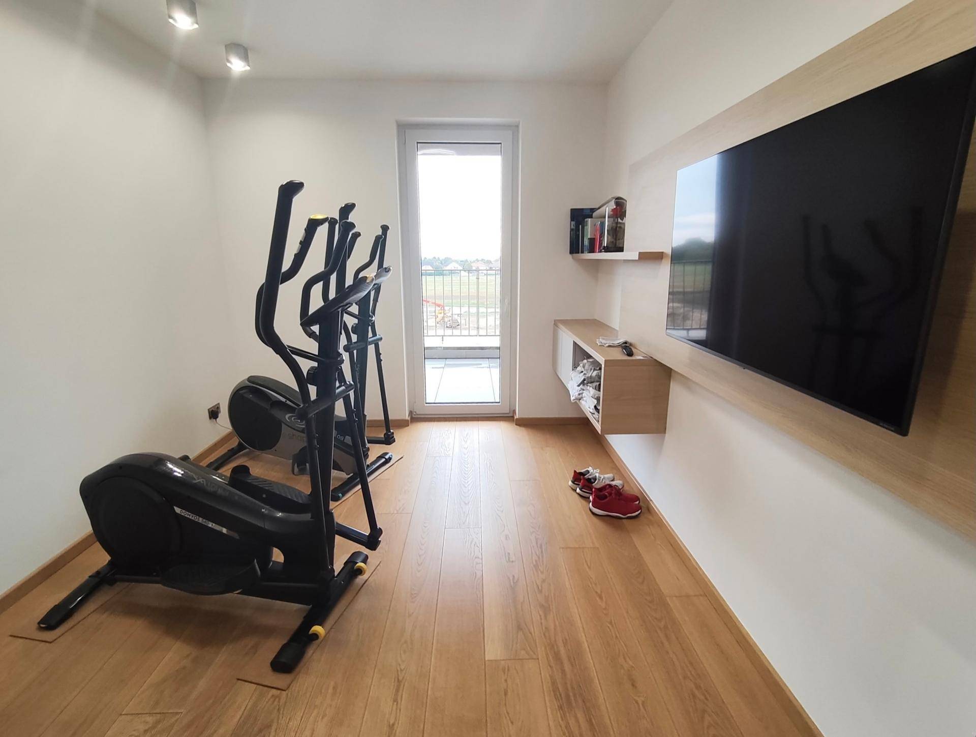 Fitnessraum mit Trainingsgeräten und Zugang zu einem Balkon.