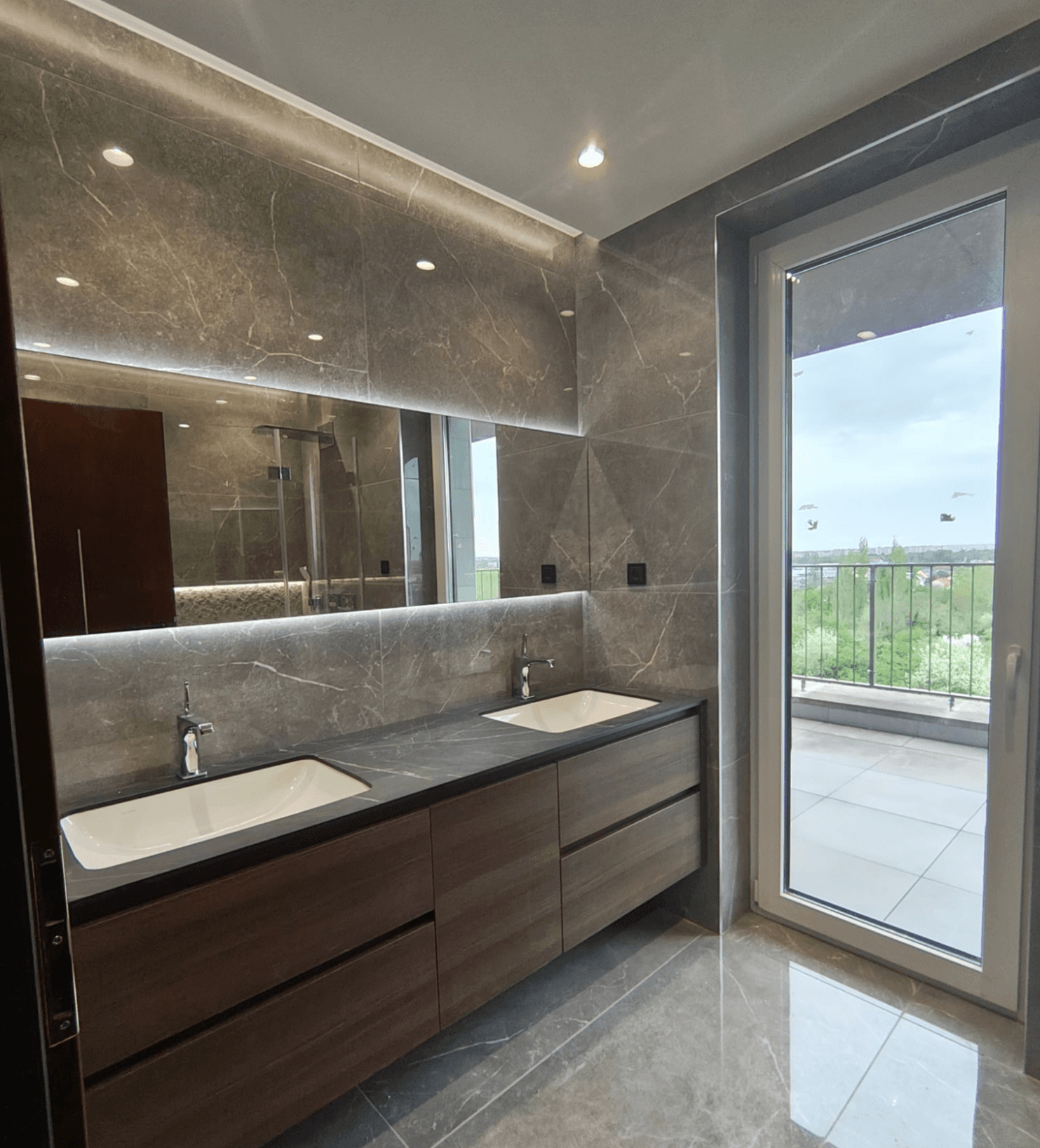Helles Badezimmer mit Doppelwaschbecken, Marmoroberflächen und Zugang zu einem Balkon.