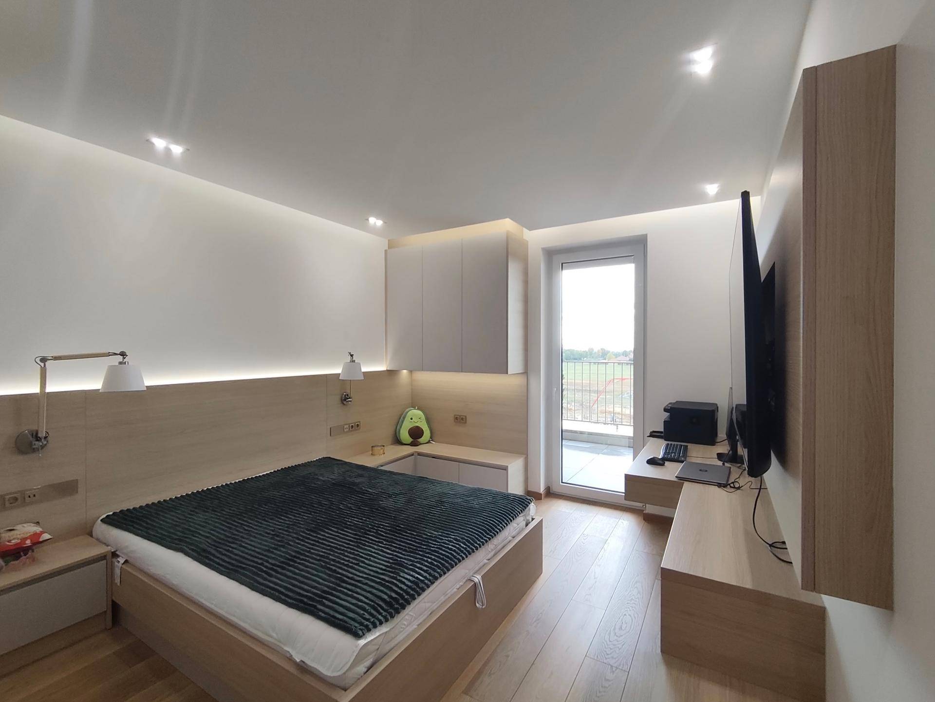 Helles Schlafzimmer mit Holzbett, integrierten Schränken und Balkonzugang.