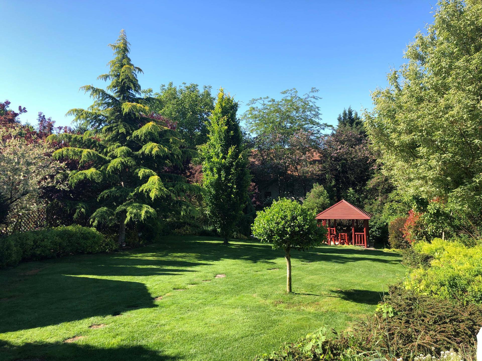 Großer, gepflegter Garten mit Rasenfläche, alten Bäumen und einem Gartenpavillon.