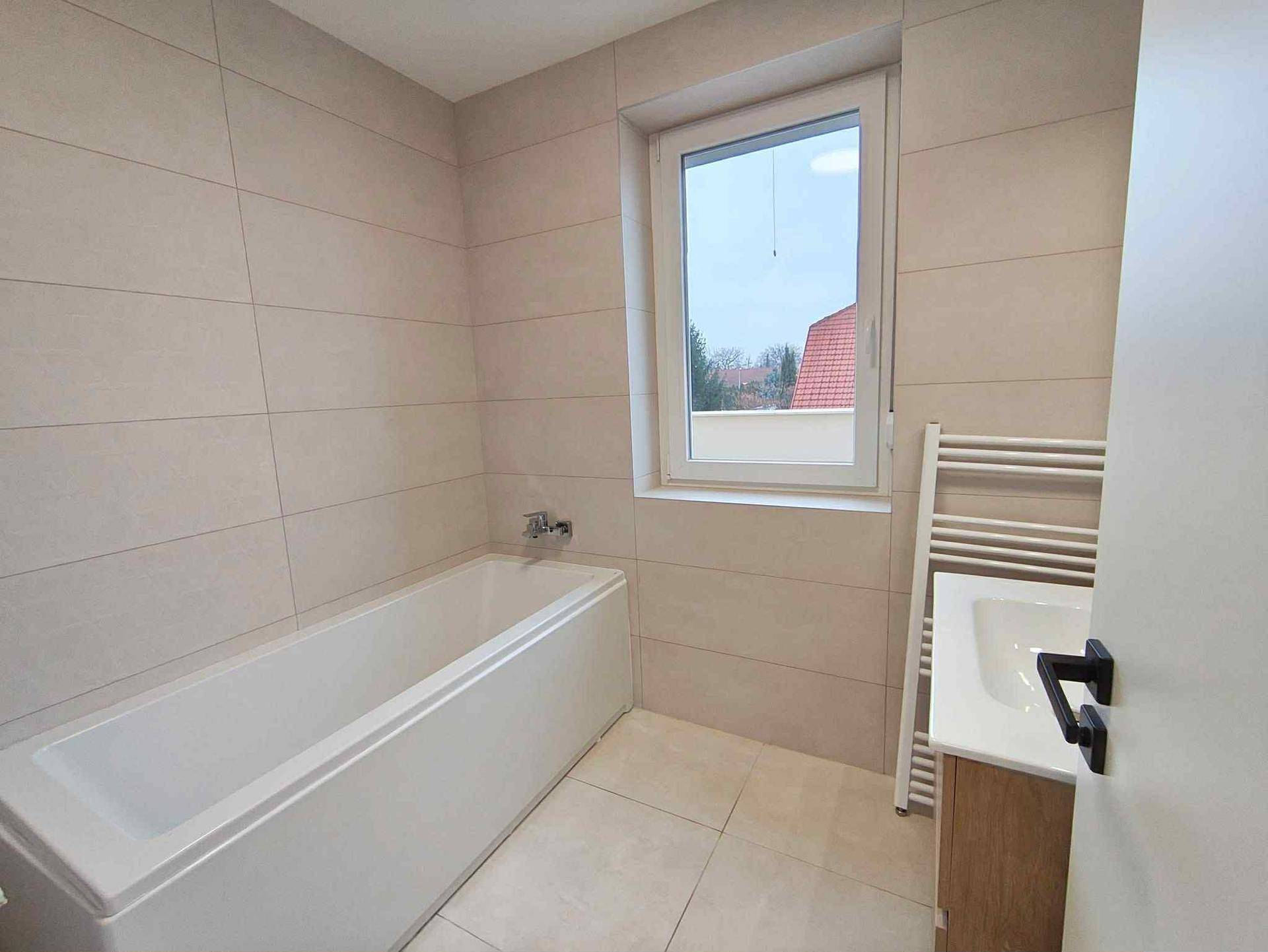 Modernes Badezimmer mit Badewanne, Fliesenboden und Fenster für natürliches Licht.