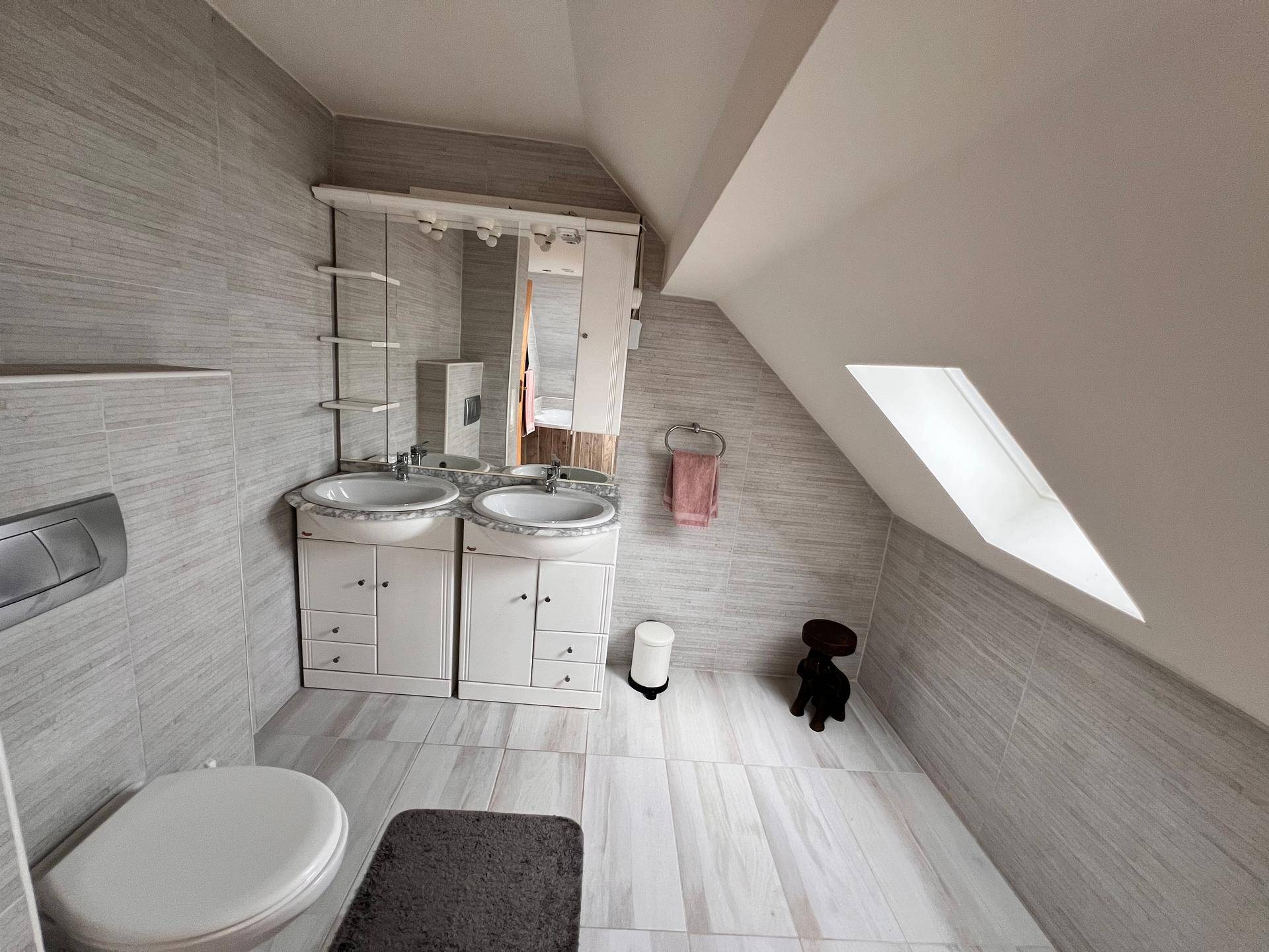Modernes Badezimmer im Dachgeschoss mit Doppelwaschbecken, WC und Spiegelschrank.