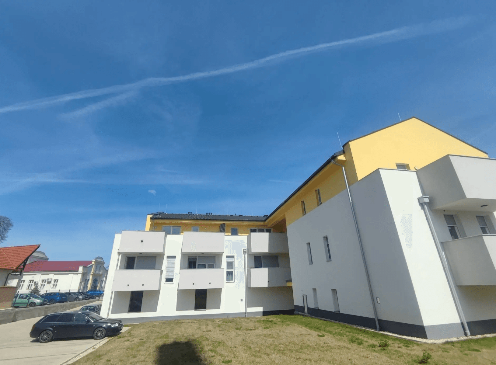 Moderne Wohnanlage mit gelber und weißer Fassade unter blauem Himmel, umgeben von Grünflächen.