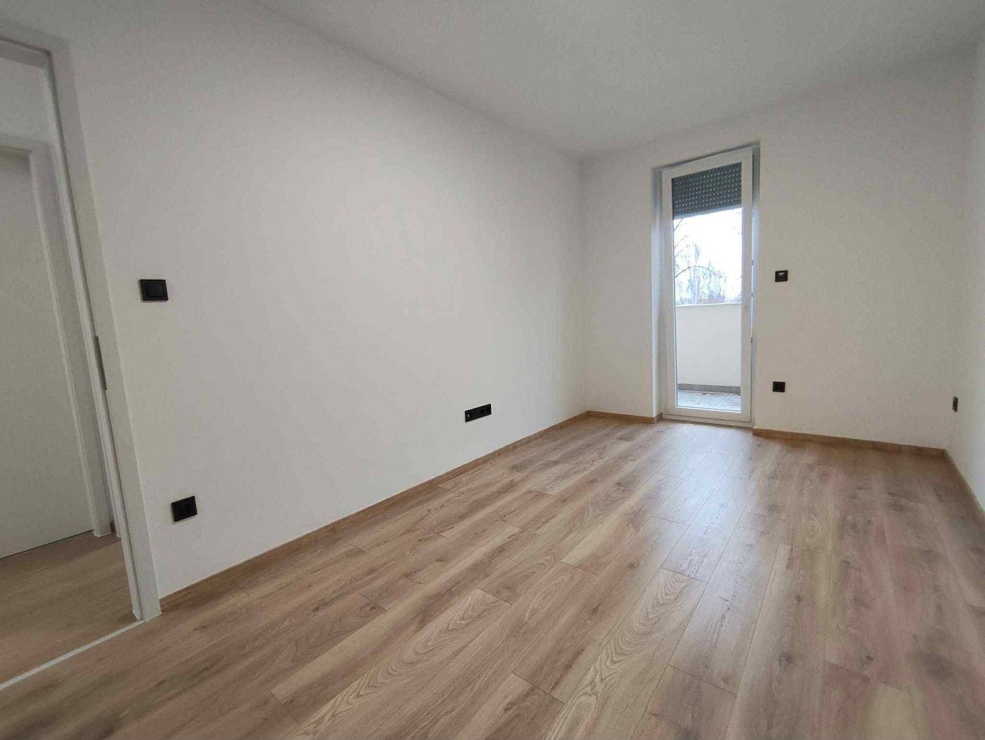 Leeres Schlafzimmer mit Holzboden und Zugang zu einem kleinen Balkon, bereit zur individuellen Gestaltung.