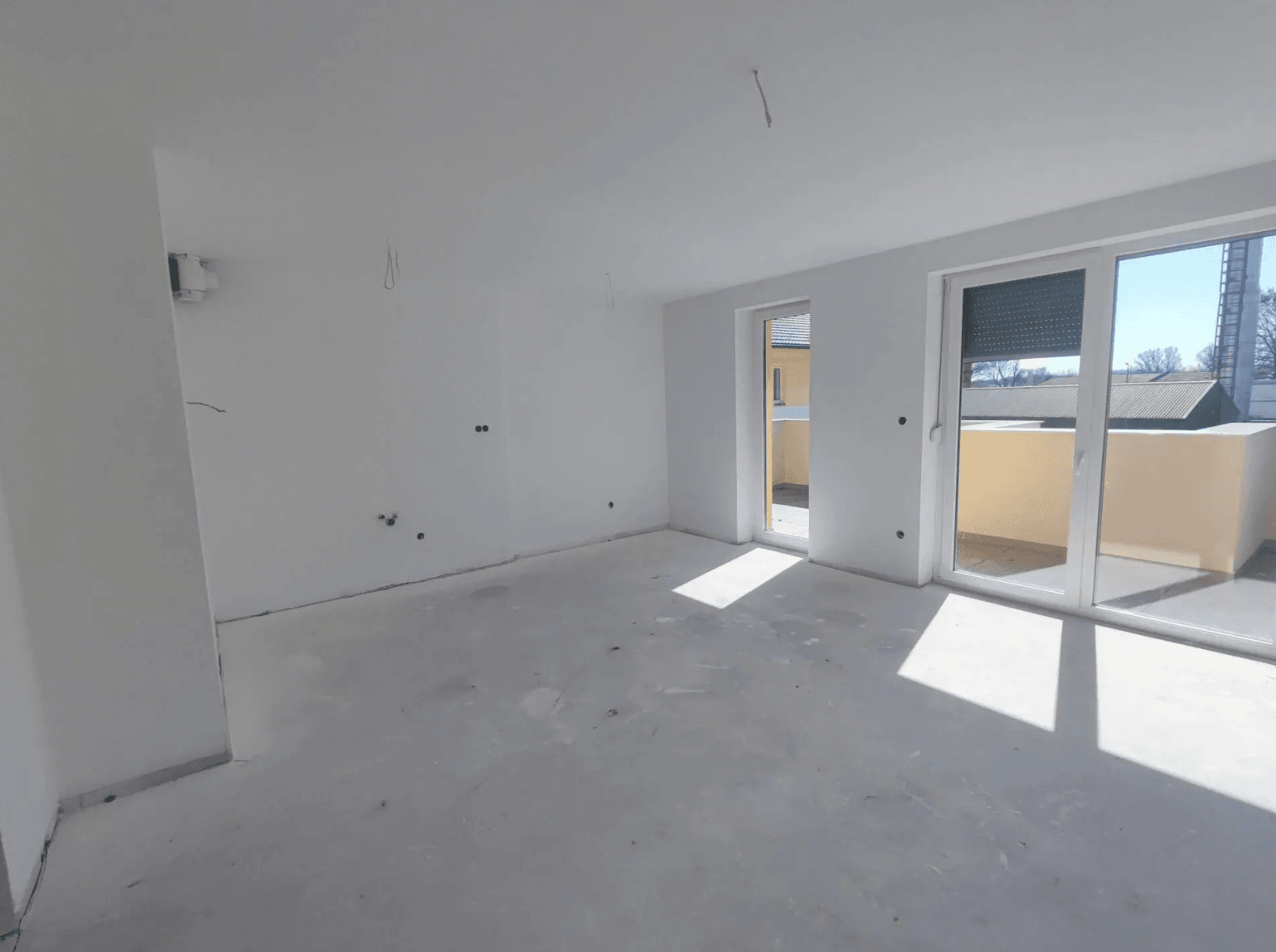 Großes, unfertiges Wohnzimmer mit Rohboden und mehreren Balkonzugängen, ideal für individuelle Gestaltung.