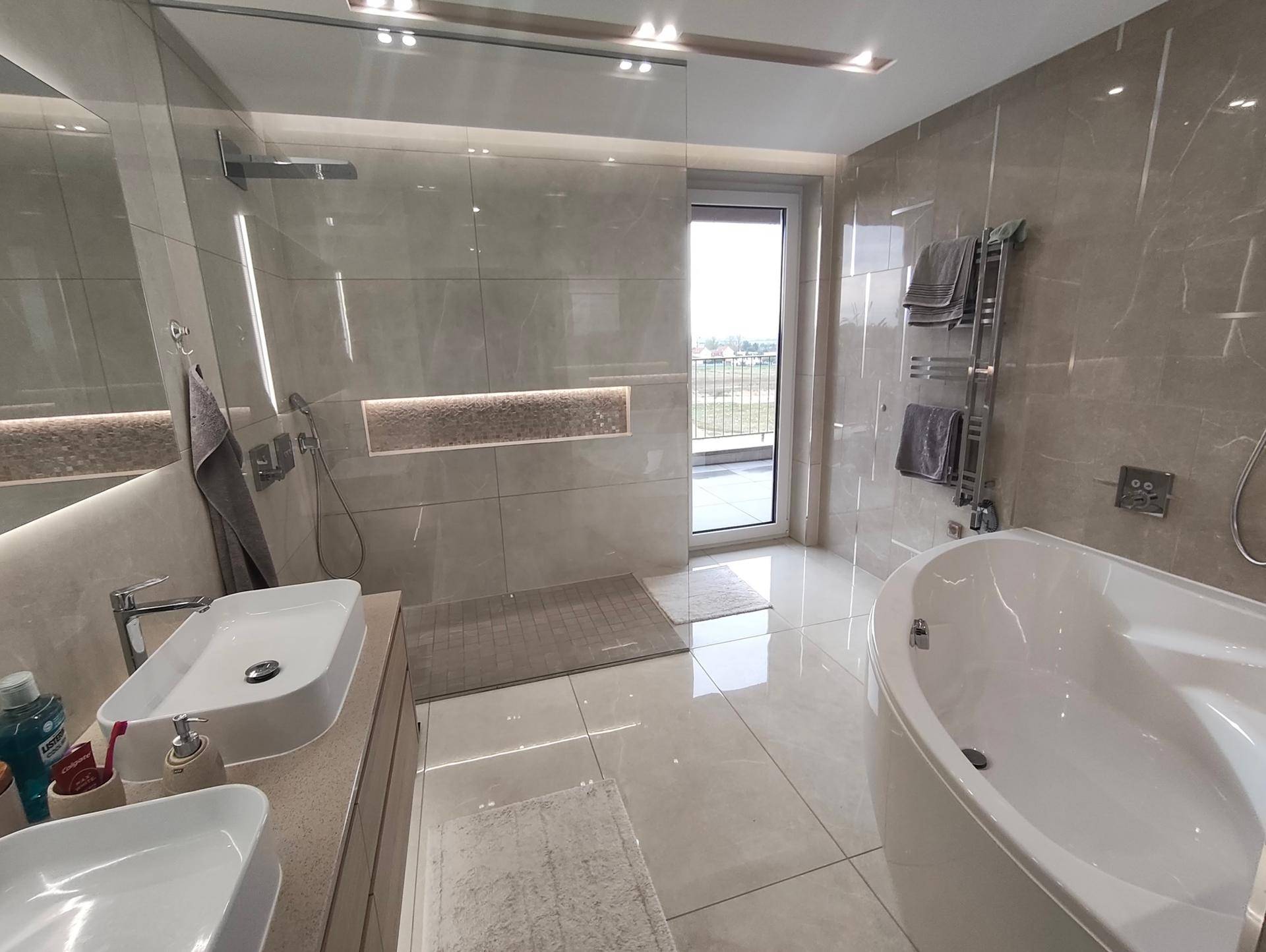 Helles Badezimmer mit Badewanne, Duschbereich und Zugang zum Balkon.