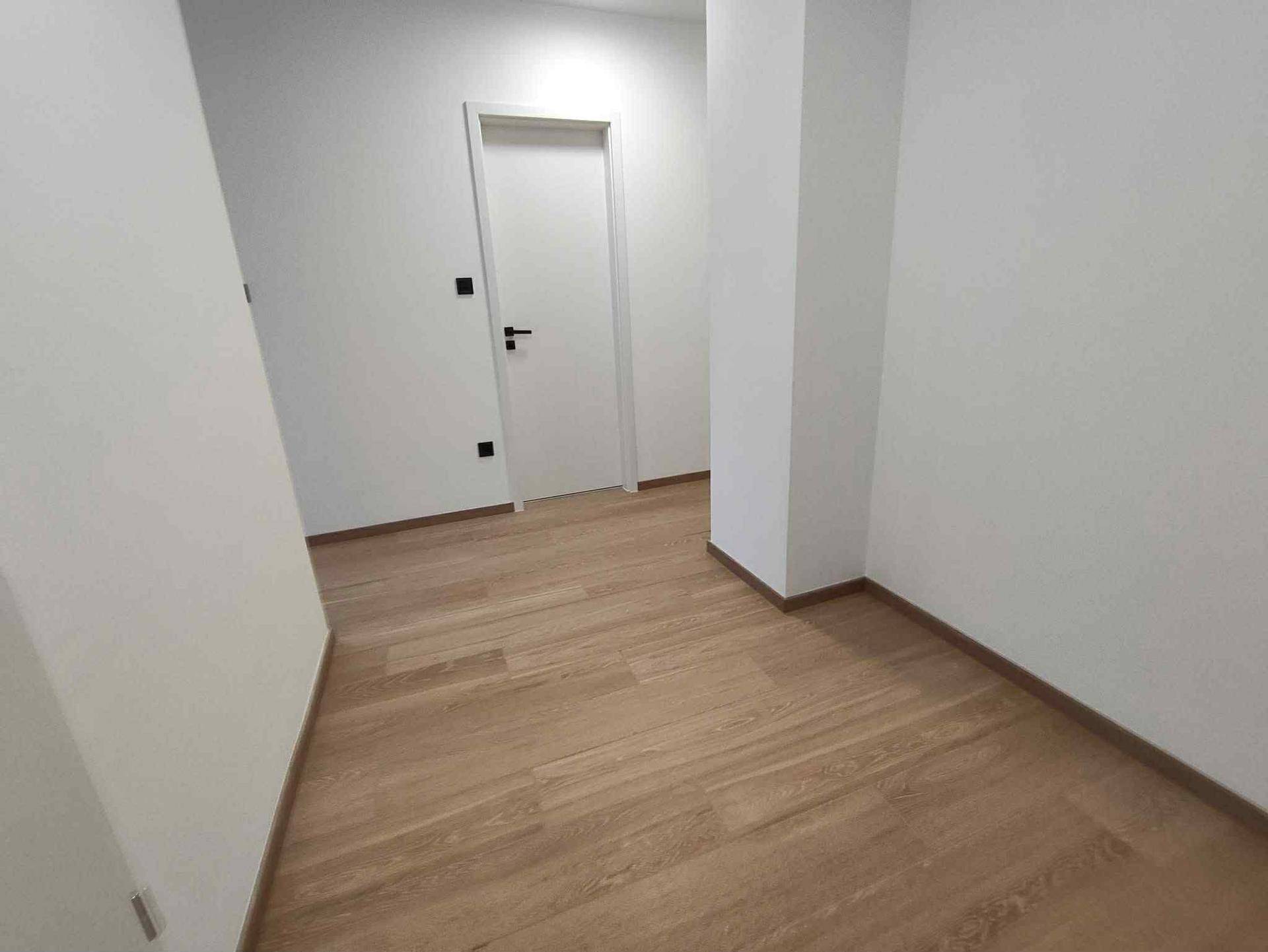 Heller Flur mit Holzboden und weißen Wänden, der zu weiteren Räumen führt.