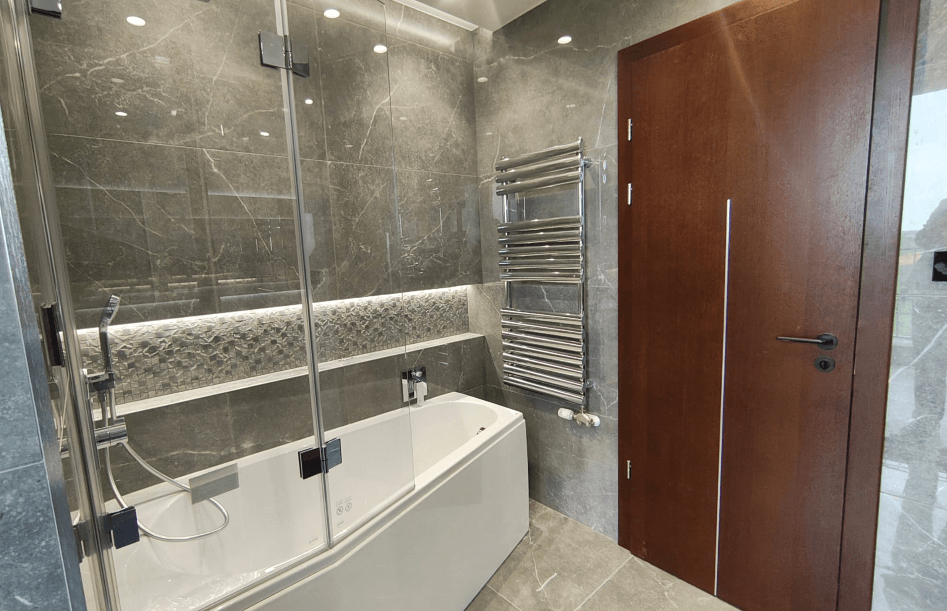 Modernes Badezimmer mit grauen Marmorfliesen, Badewanne und beheiztem Handtuchhalter.