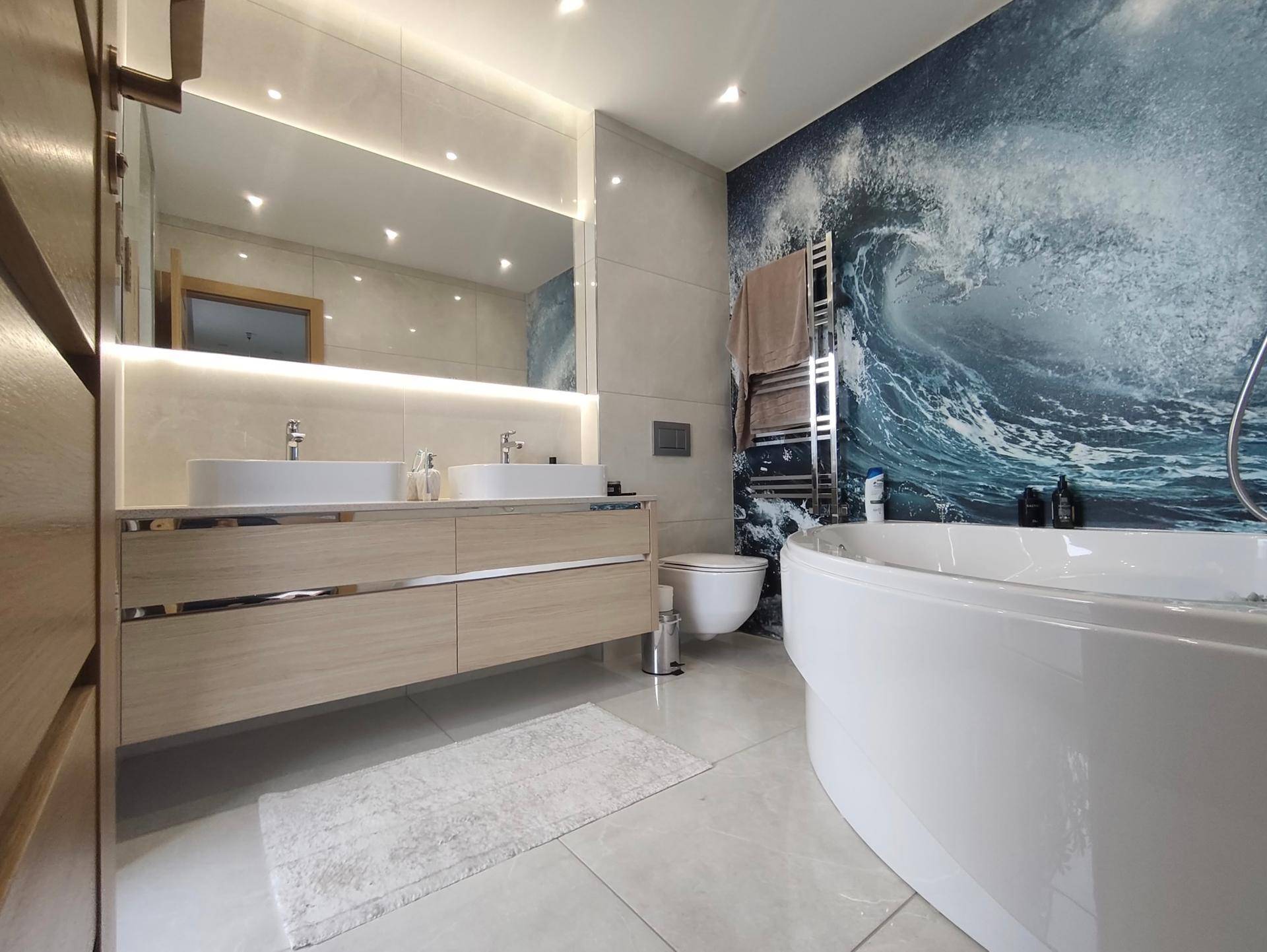 Modernes Badezimmer mit Doppelwaschbecken, Badewanne und auffälliger Wellen-Tapete.