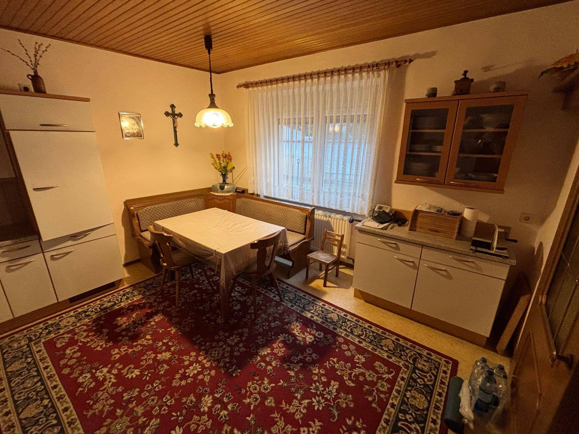 Gemütliche Wohnküche mit Holzbalkendecke, weißer Küchenzeile und einem Essbereich am Fenster.