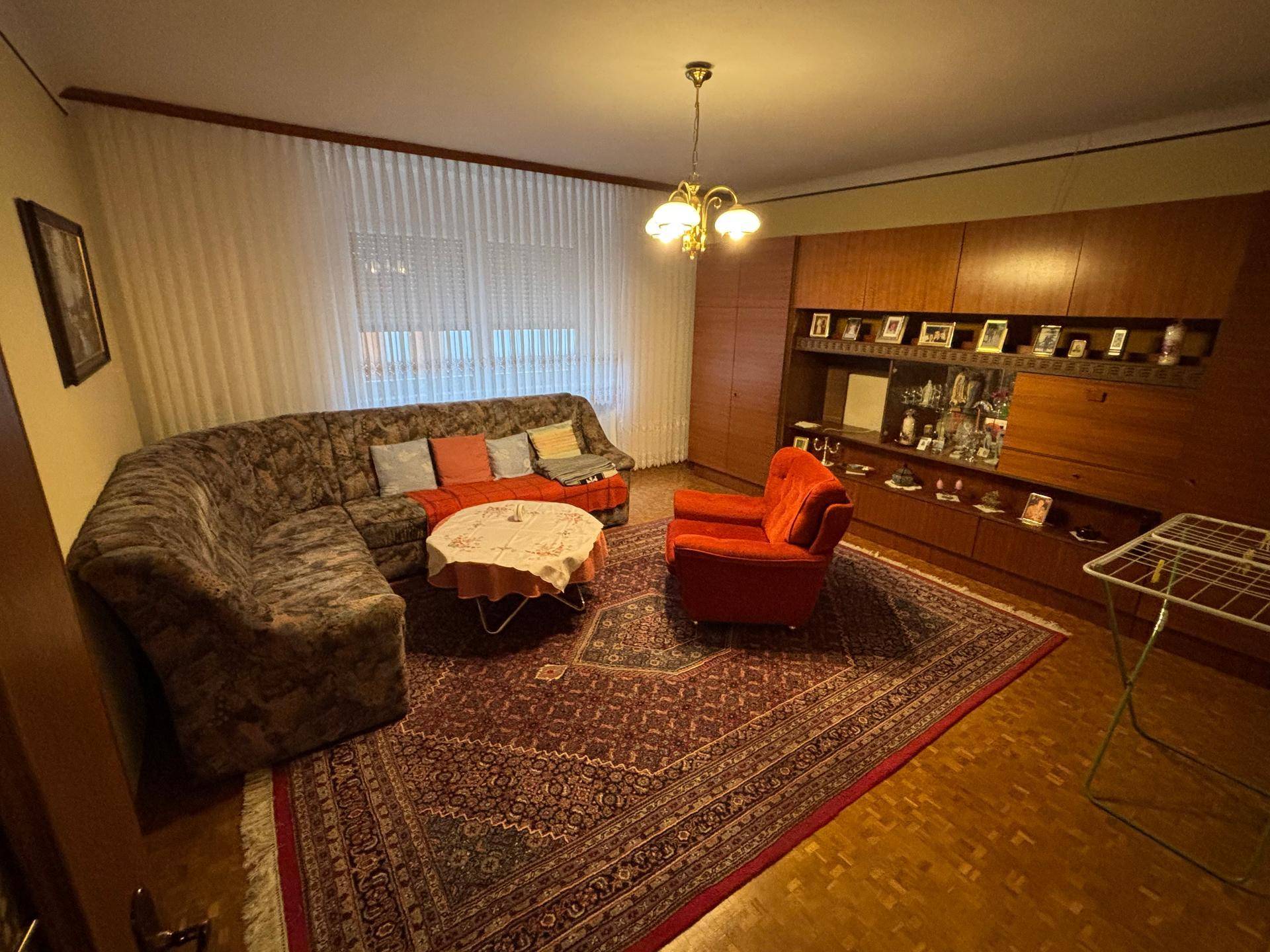 Wohnzimmer mit Teppichboden, bequemer Sitzecke und einer großen Holzschrankwand im Vintage-Stil.