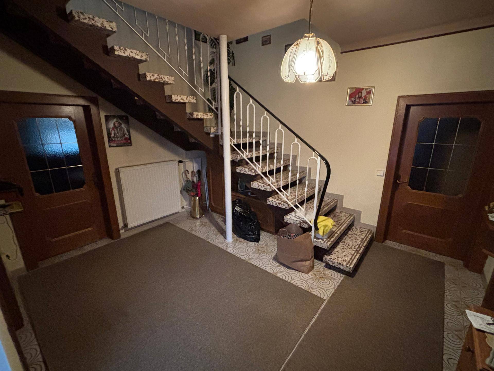 Geräumiger Flur mit Treppe, Teppichboden und zwei Holztüren, die zu weiteren Räumen führen.