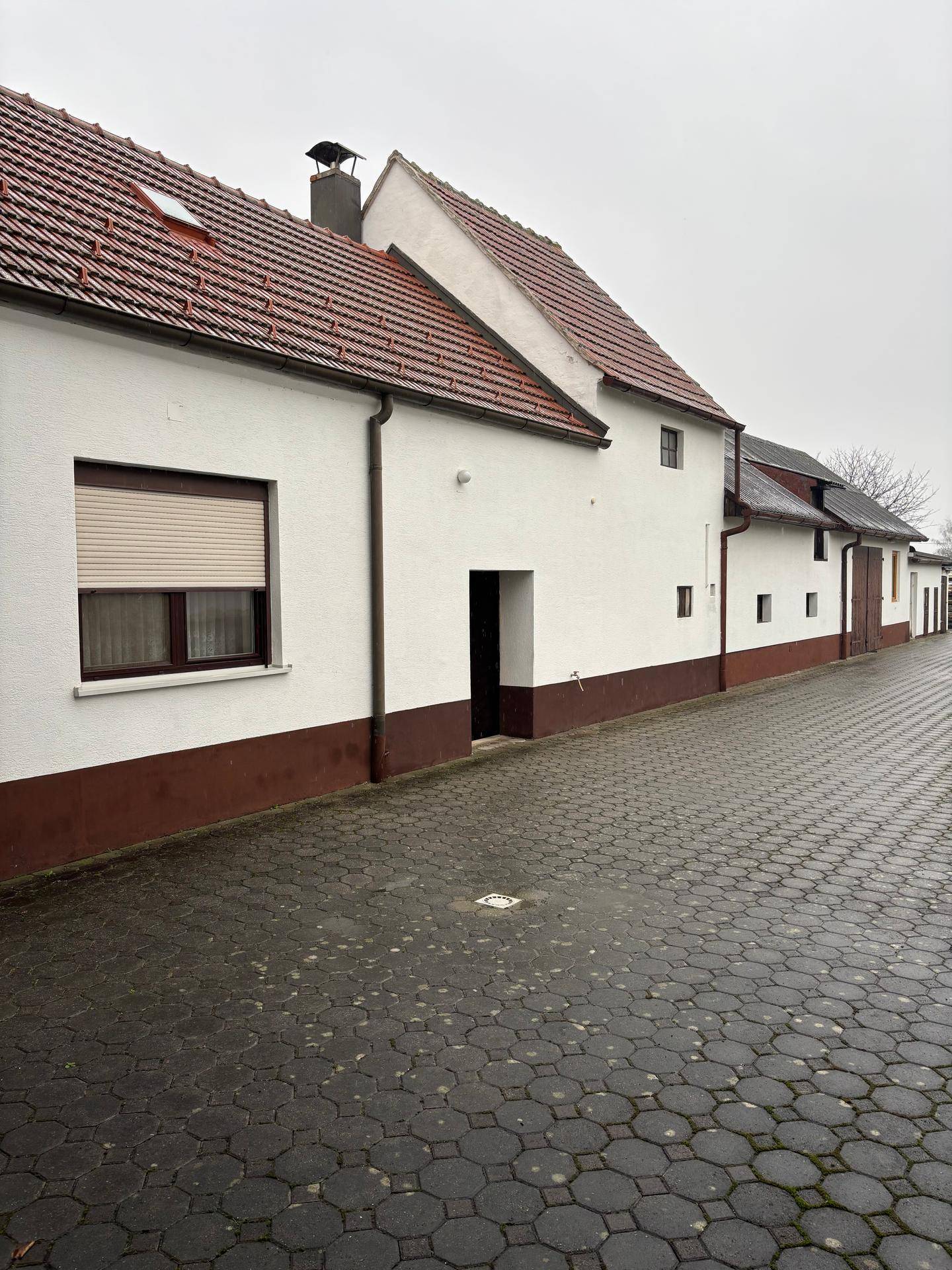 Langes, weiß getünchtes Gebäude mit rotem Ziegeldach und gepflastertem Weg daneben.