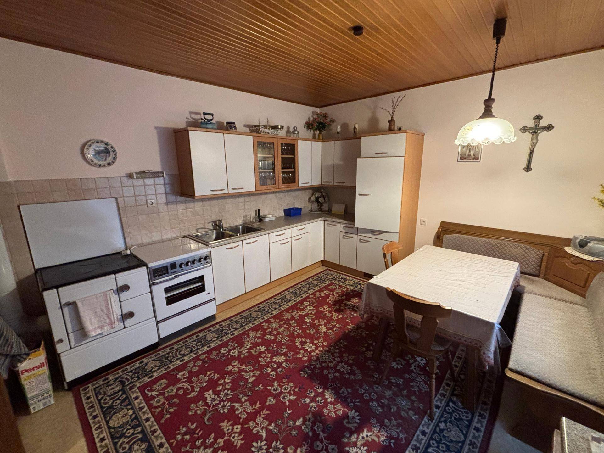 Traditionelle Küche mit Holzbalkendecke, weißer Einbauküche und einem Esstisch mit Eckbank.