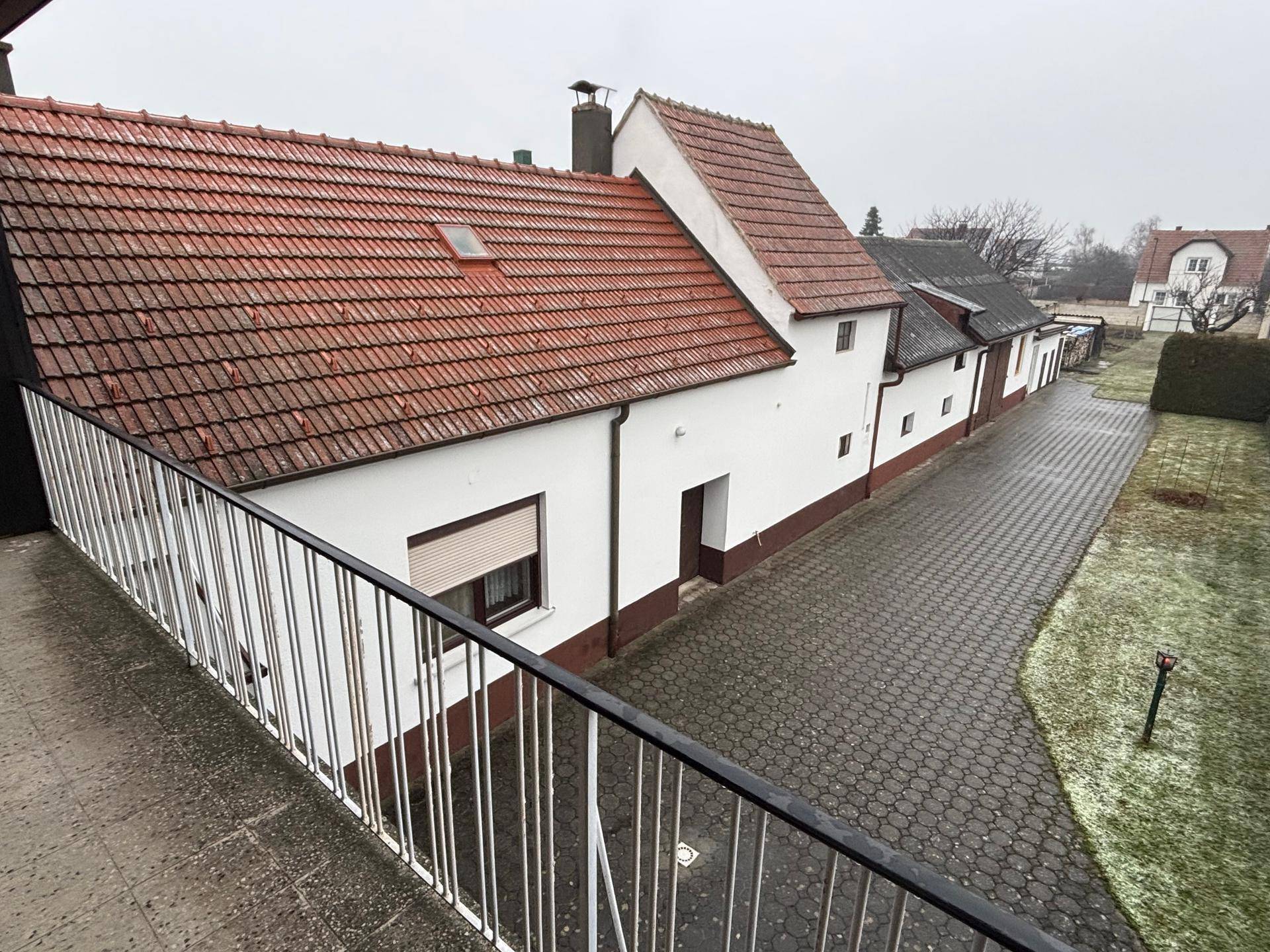 Blick vom Balkon auf den gepflasterten Hof und die angrenzenden Gebäude mit roten Ziegeldächern.