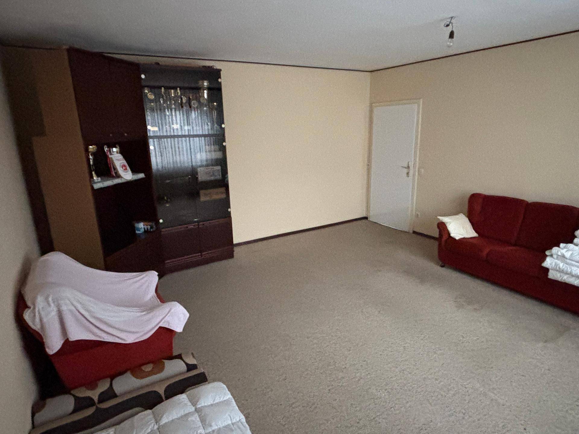 Geräumiges Zimmer mit Teppichboden, rotem Sofa und einem Schrank, der Stauraum bietet.