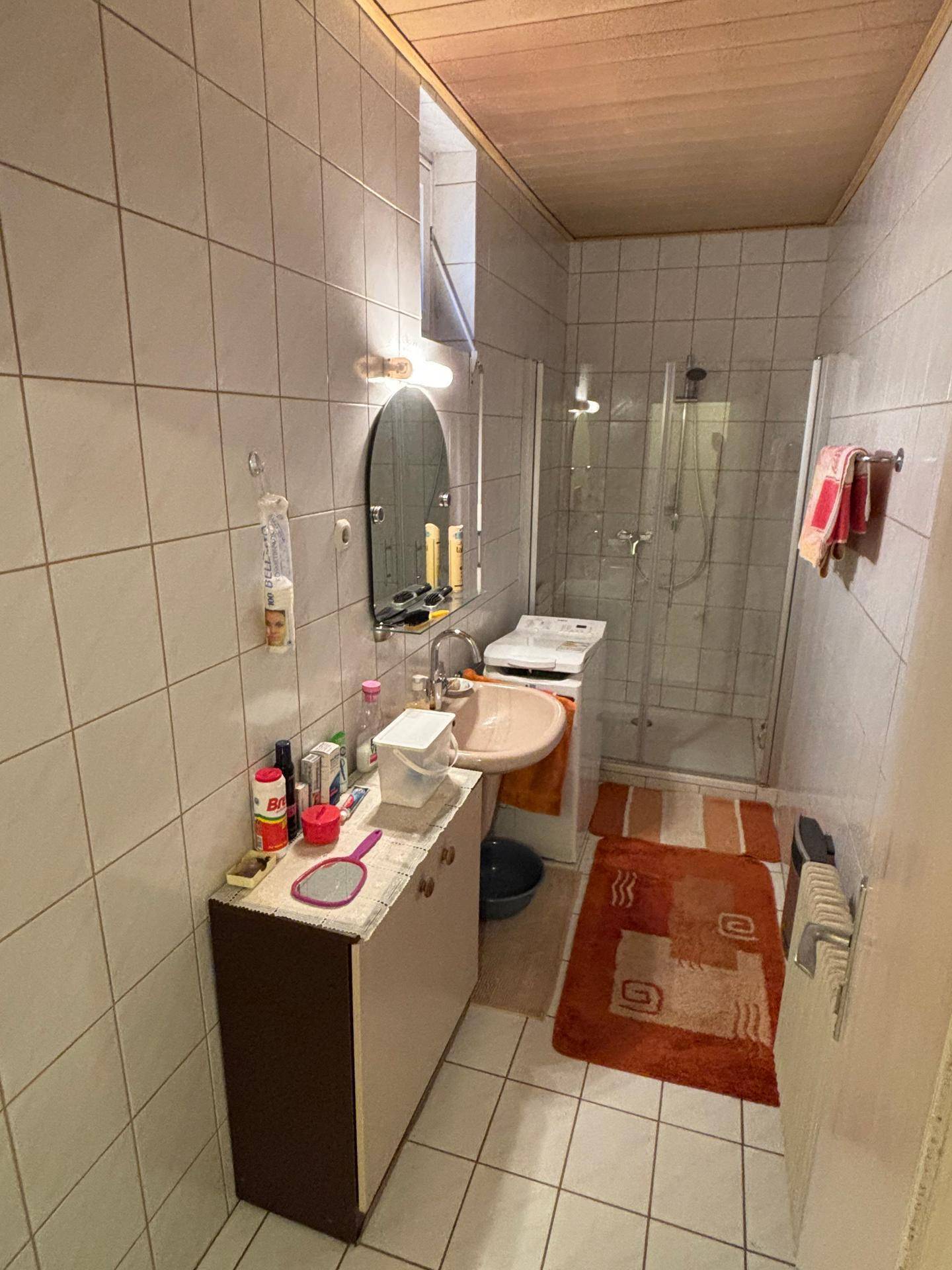 Badezimmer mit Duschkabine, Waschbecken und Waschmaschine, ausgestattet mit weißen Wandfliesen.