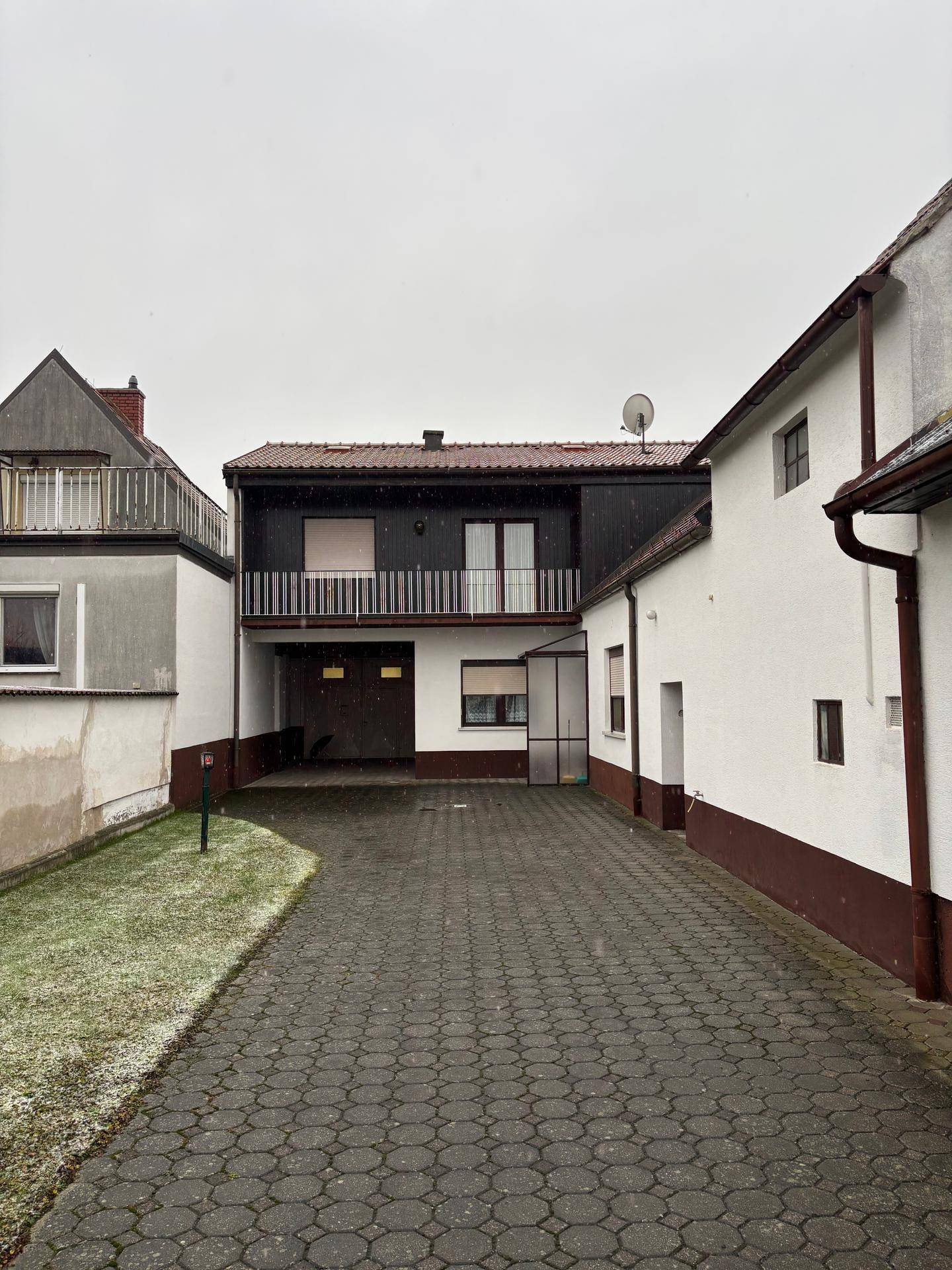 Blick auf den hinteren Bereich des Anwesens mit mehreren Gebäuden, gepflastertem Hof und Rasenflächen.