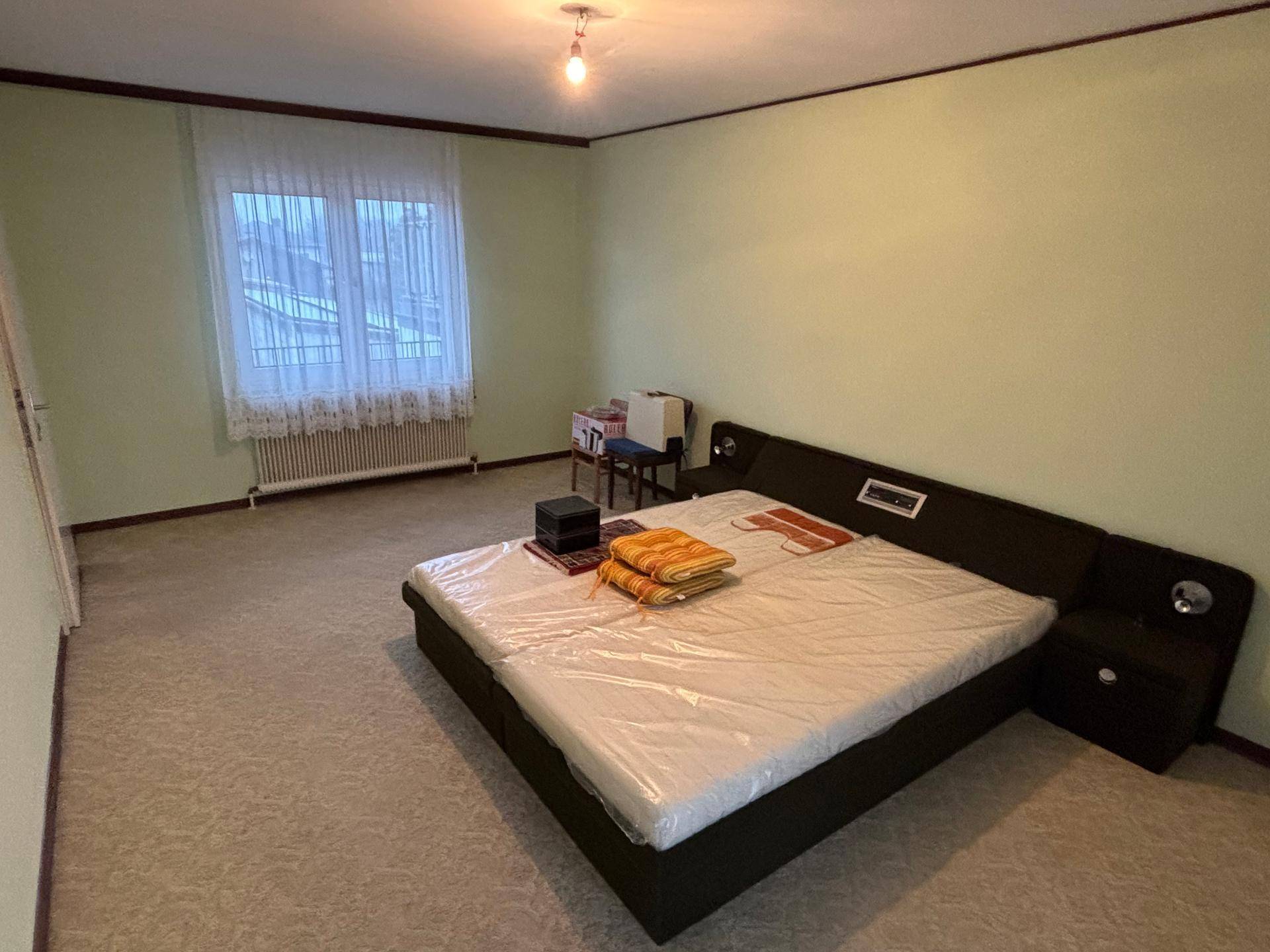 Helles Schlafzimmer mit Teppichboden, Doppelbett und einem großen Fenster, das viel Licht hereinlässt.