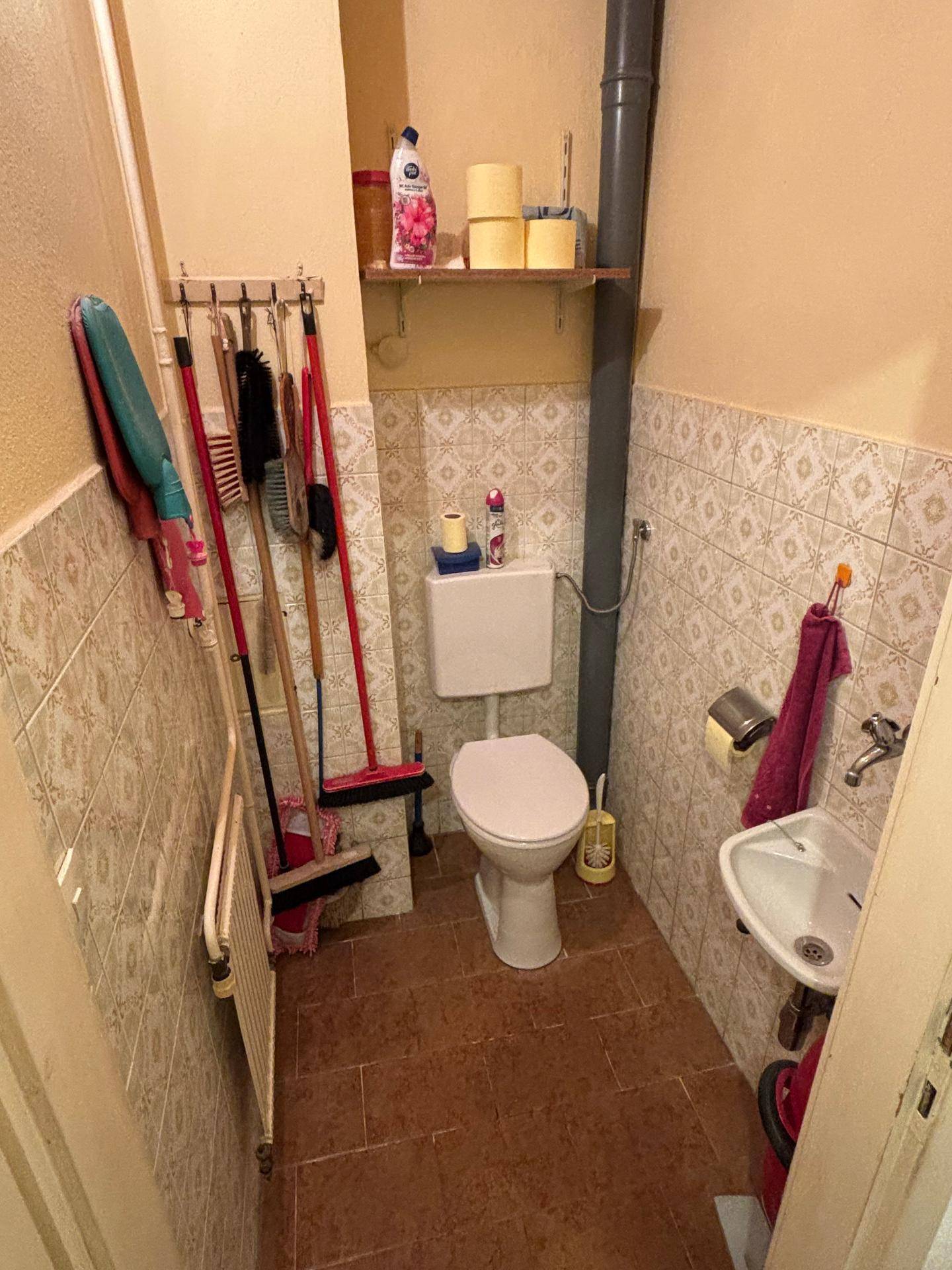 Kleines Gäste-WC mit Fliesenboden, Wandfliesen und einem Waschbecken in einfacher Ausführung.