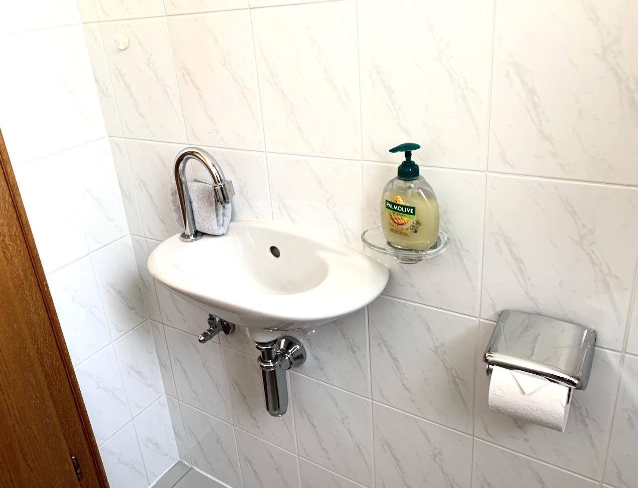 Waschbecken in einem kleinen Badezimmer mit weißen Fliesen und Seifenspender.