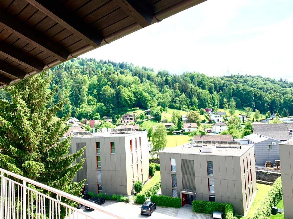 Blick von einem Balkon auf moderne Gebäude und eine grüne Hügellandschaft.