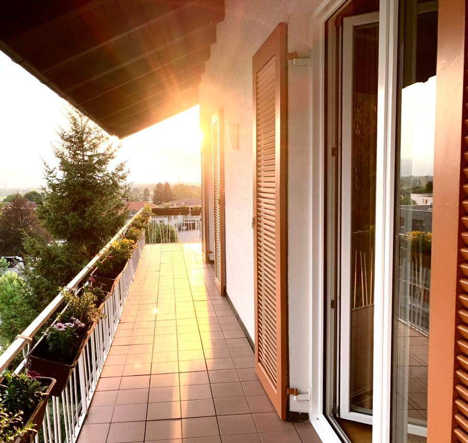 Sonniger Balkon mit Fliesenboden, Blumenkästen und weitem Blick in die Landschaft.