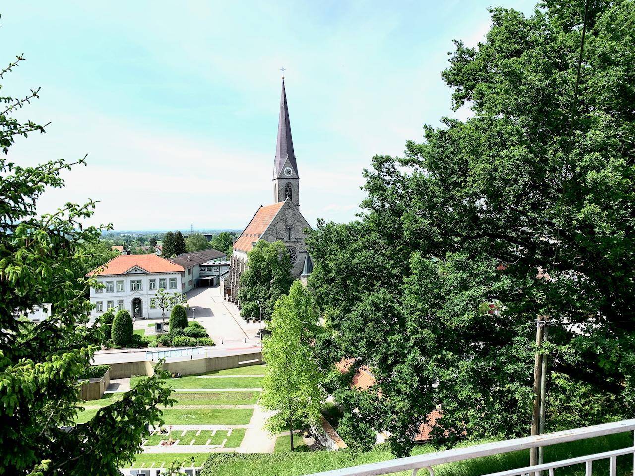 Panoramablick auf eine Kirche mit hohem Turm und umliegende grüne Parklandschaft.