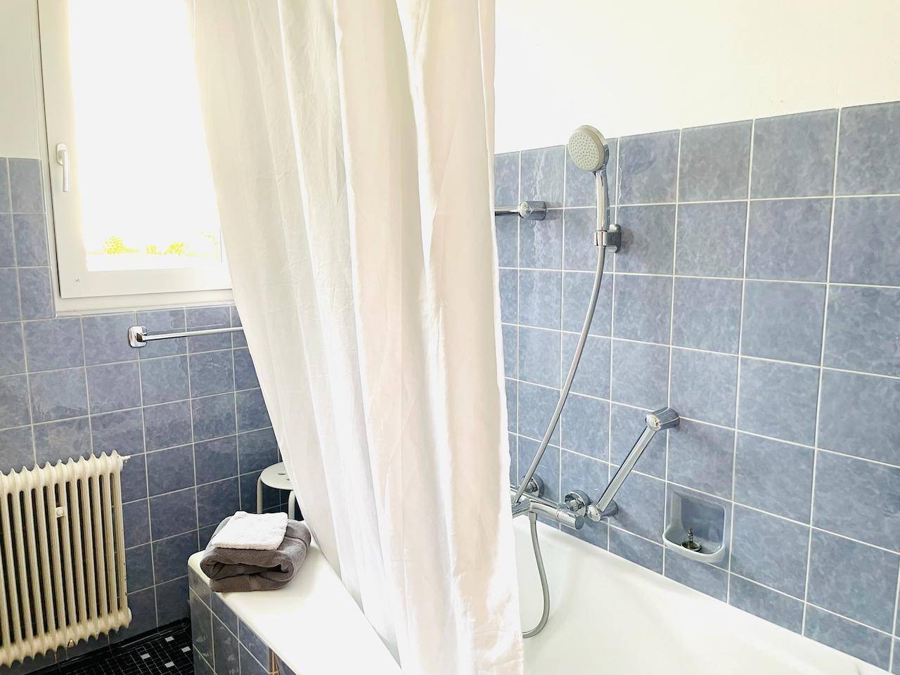 Badezimmer mit Badewanne, Duschvorhang und blauen Wandfliesen.