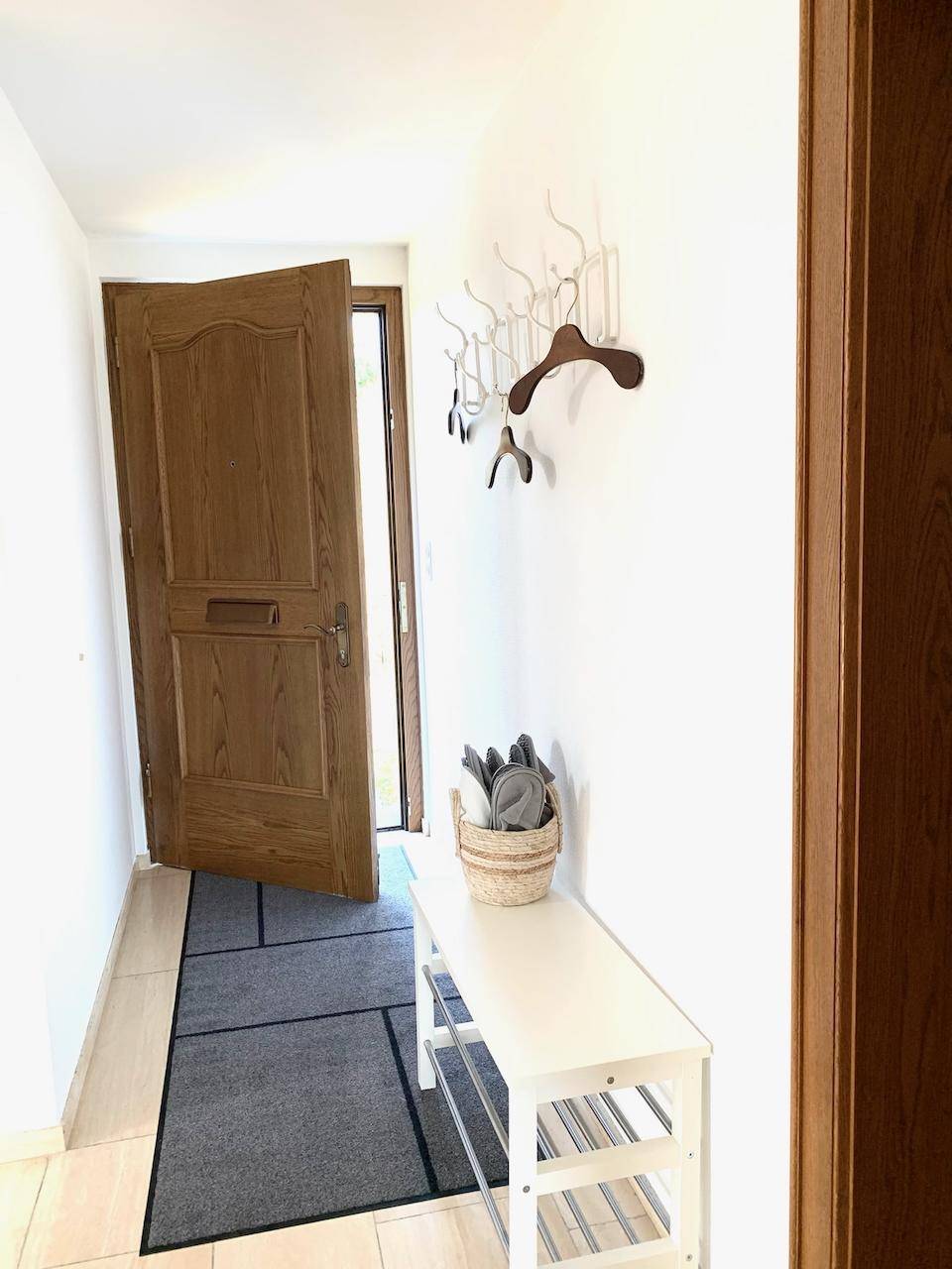 Heller Eingangsbereich mit Holztür, Garderobe und Schuhbank.