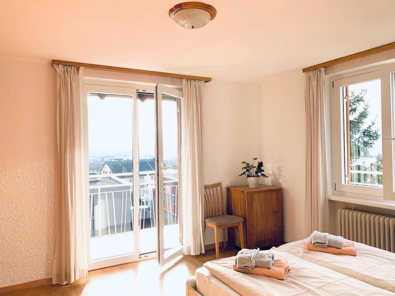 Helles Schlafzimmer mit Holzboden, Balkonzugang und Blick auf die Umgebung.