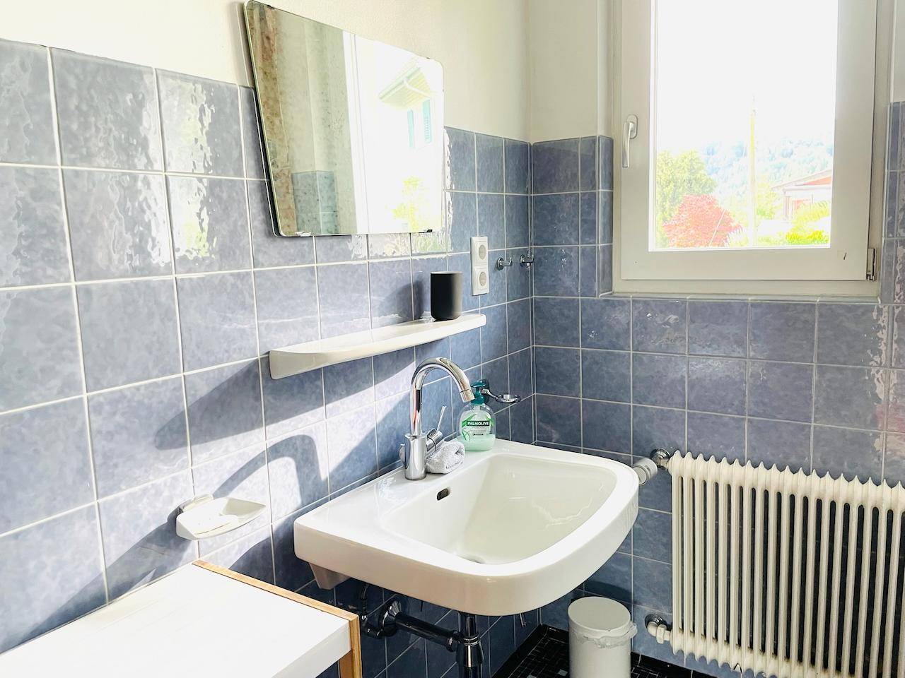 Badezimmer mit blauen Fliesen, Waschbecken, Spiegel und Fenster.