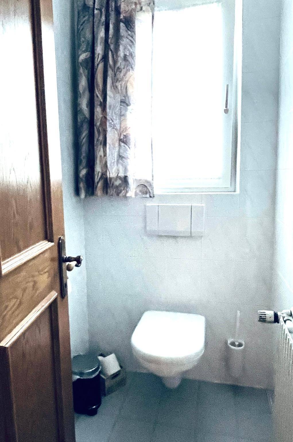 Kleines WC mit Toilette, Fenster und hellgrauen Fliesen.