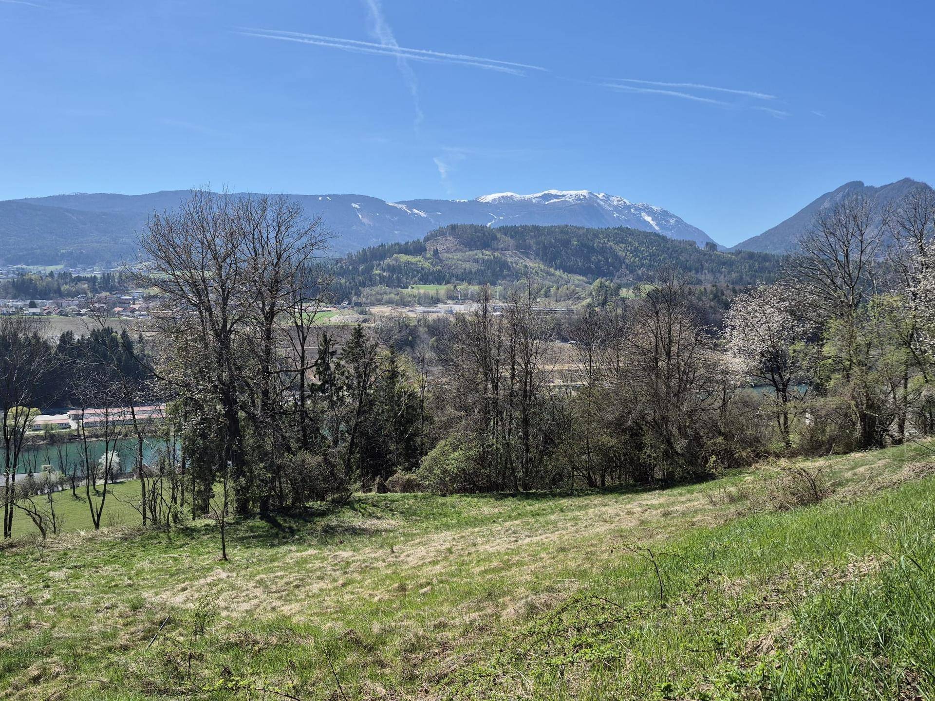Idyllische Frühlingslandschaft mit weitem Blick auf einen Fluss, eine Stadt und die schneebedeckten Berge.