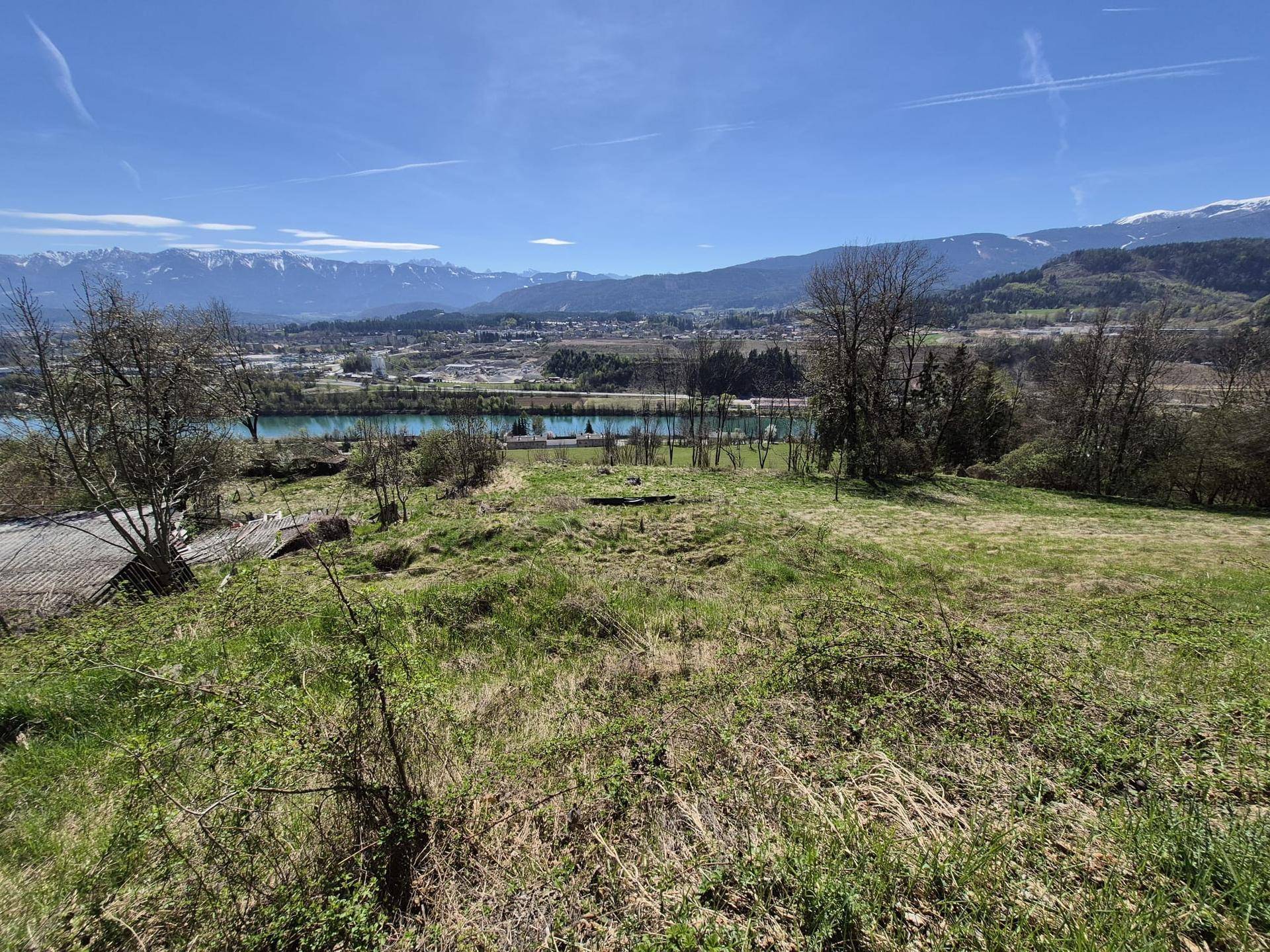 Helle Frühlingslandschaft mit weitem Blick auf einen Fluss, eine Stadt und die majestätischen Berge am Horizont.