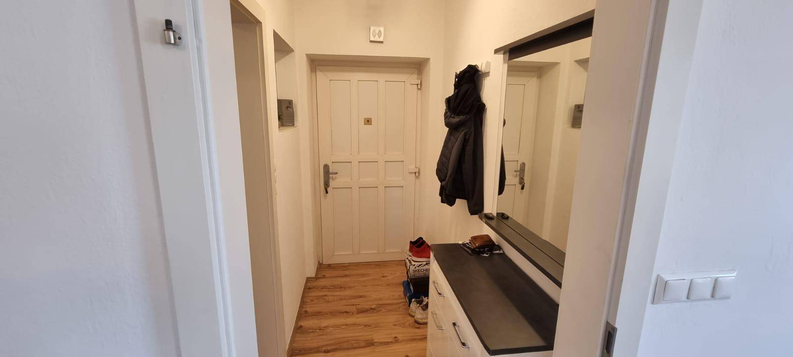 Heller Flur mit Holzboden, Spiegel und Garderobenbereich.