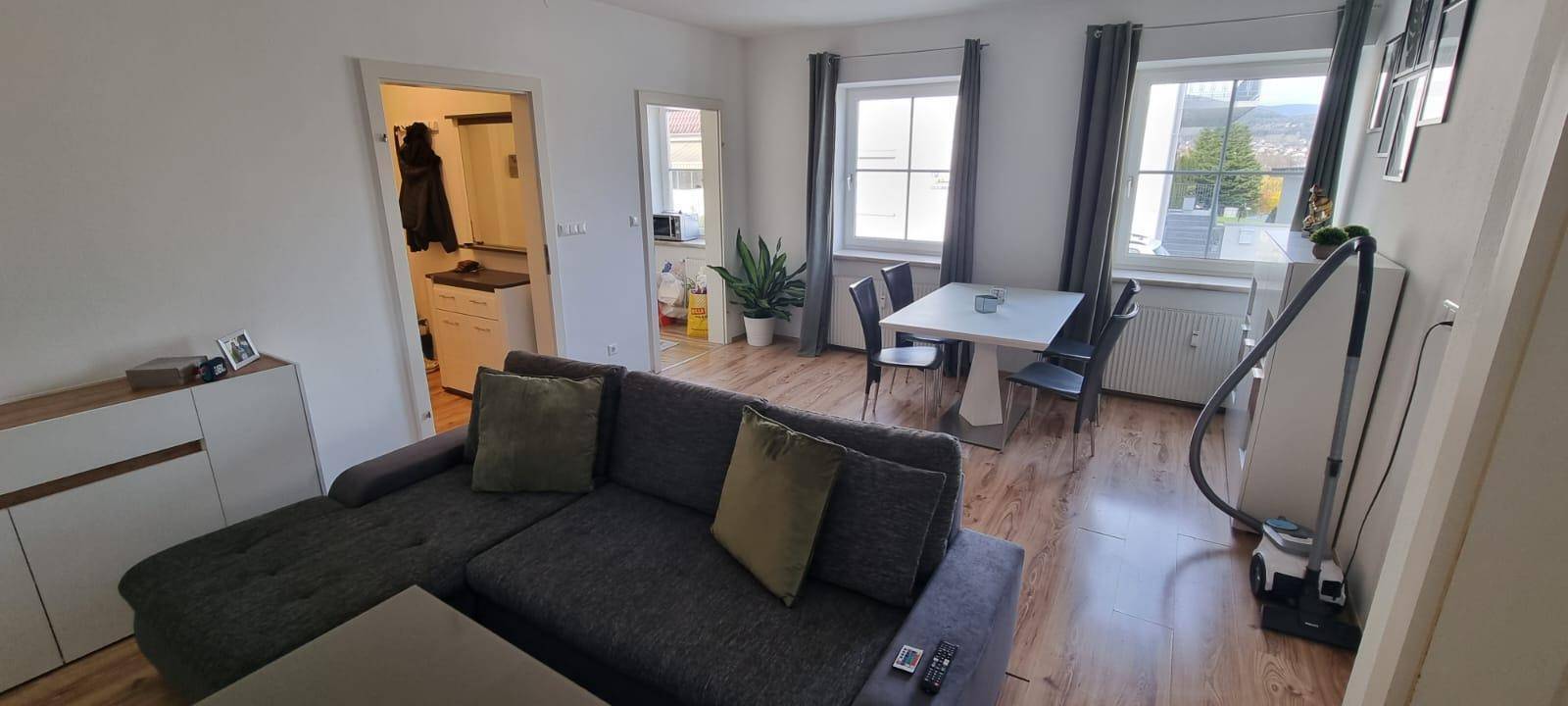 Gemütlicher Wohn- und Essbereich mit Holzboden, großem Fenster und Sofa.