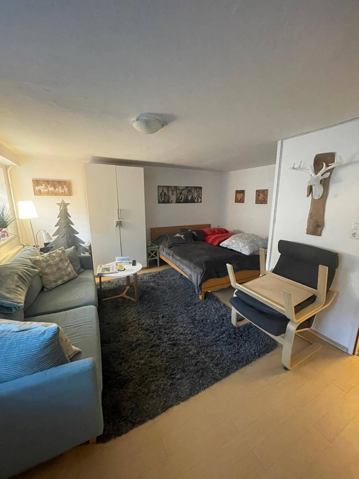 Gemütlicher Wohnbereich mit Sofa, Teppich und einem Doppelbett im Hintergrund.