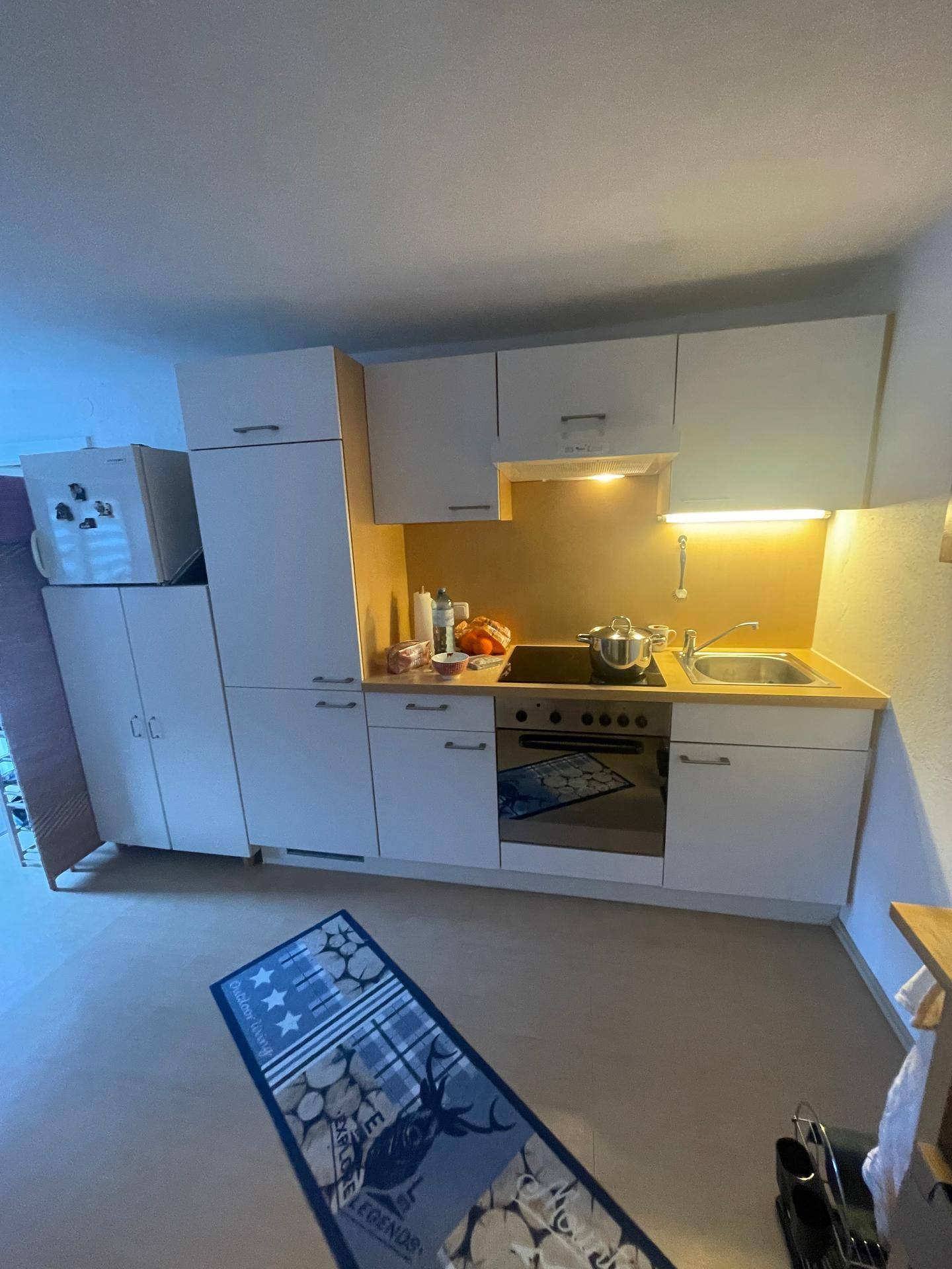 Kompakte Küchenzeile mit weißen Schränken, integrierten Geräten und Holzarbeitsplatte.