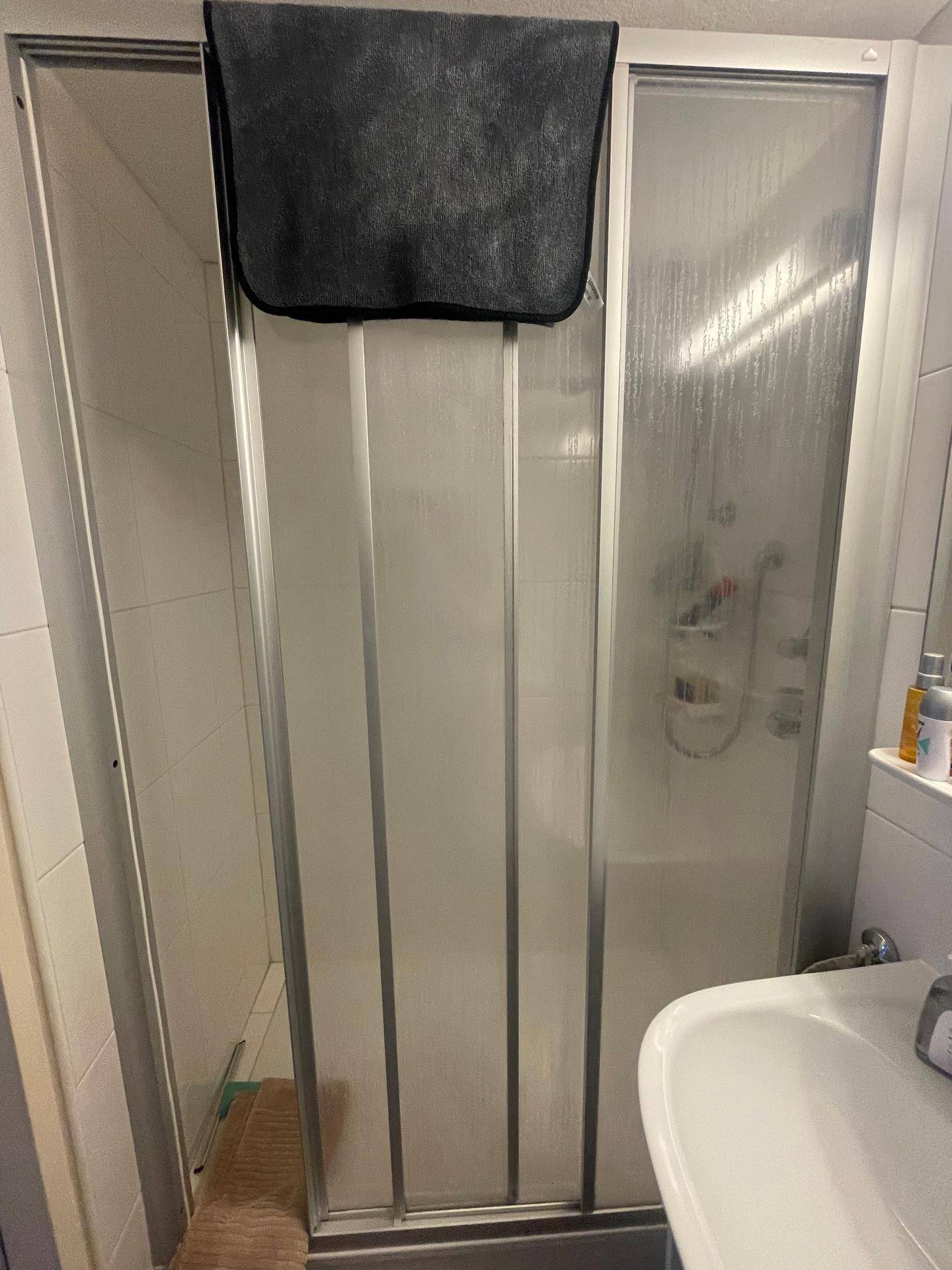 Duschbereich im Badezimmer mit Falttür und weißen Fliesen.