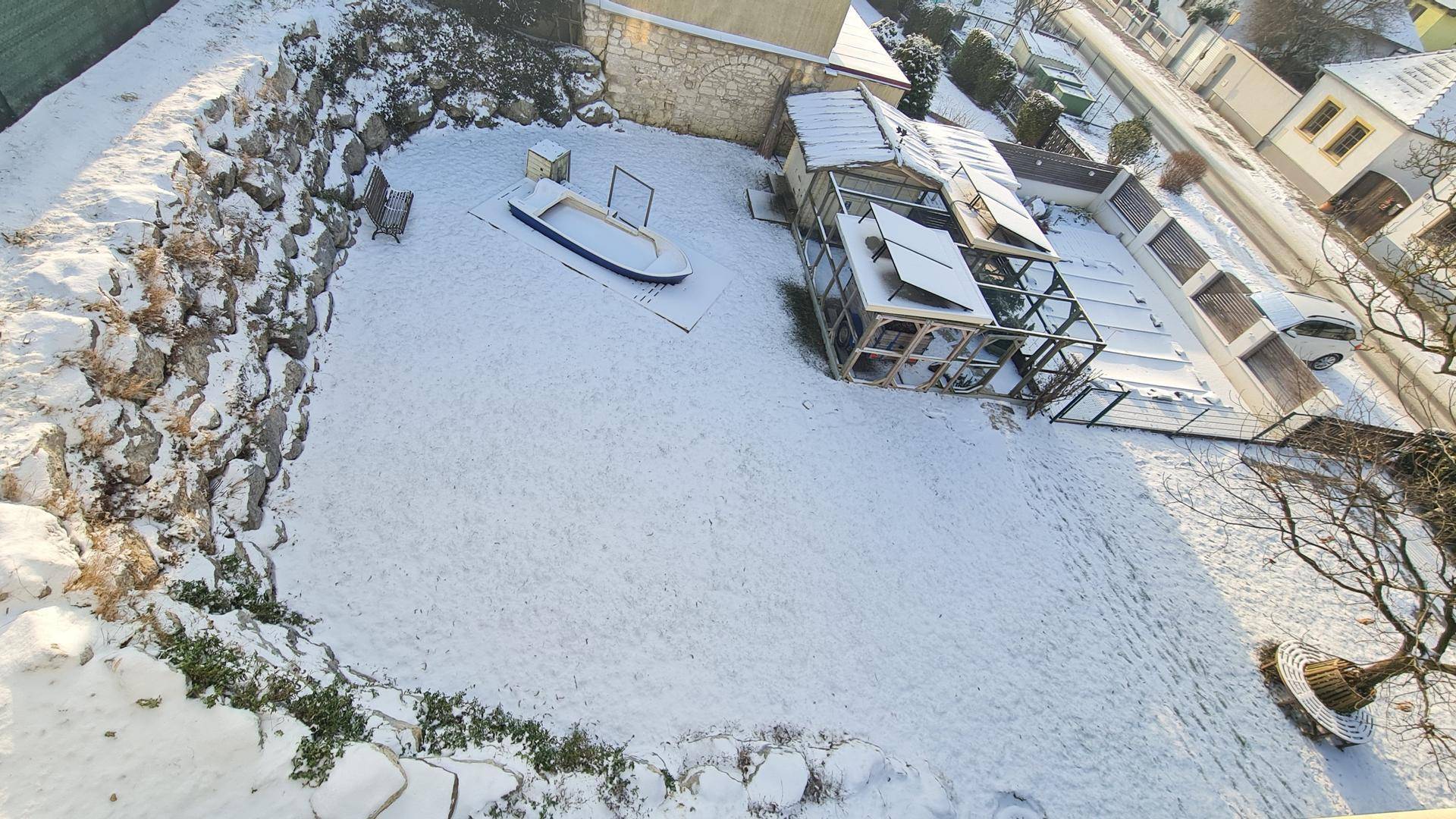 Verschneiter Gartenbereich mit Felswand, Spielgeräten und Blick auf die Umgebung.