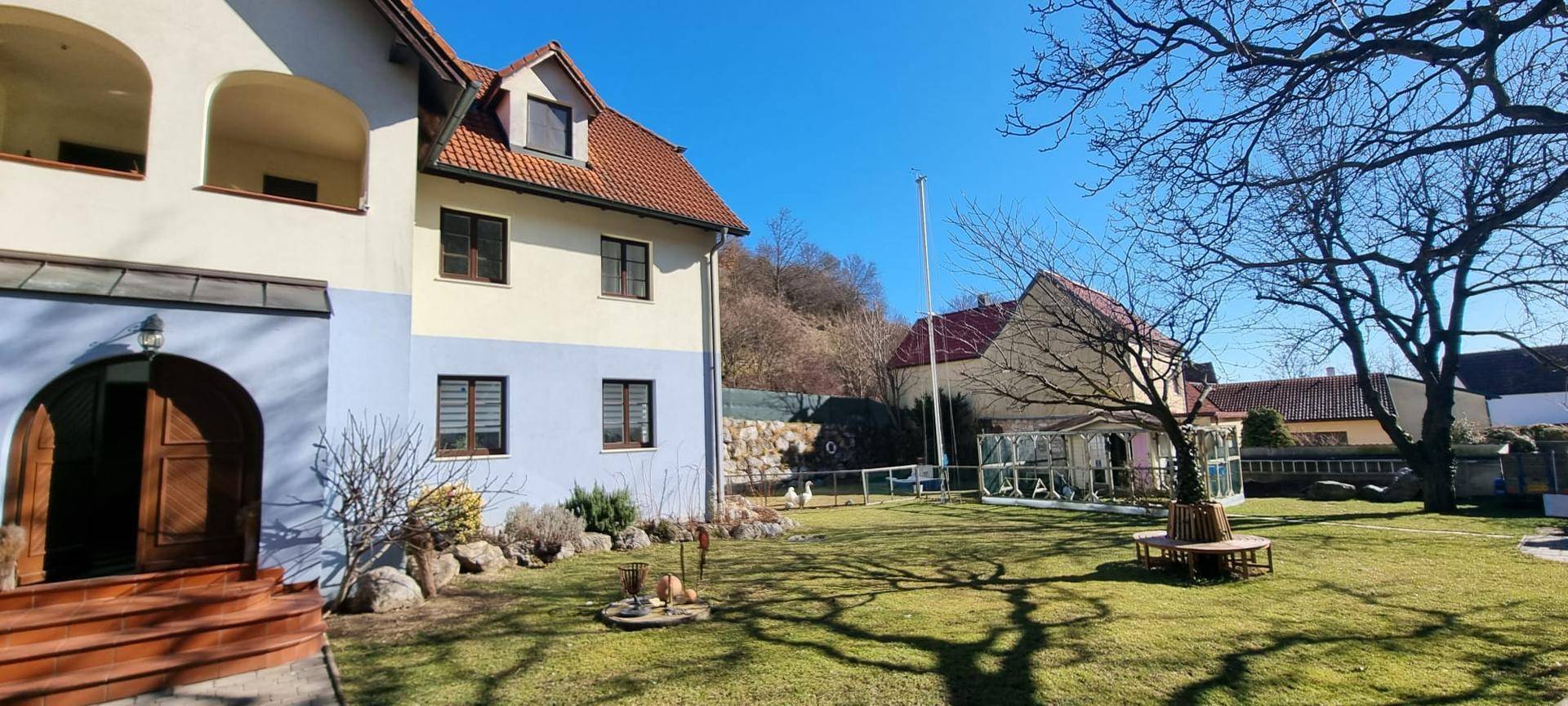 Großer Gartenbereich mit Rasen, Bäumen und Blick auf das traditionelle Haus.