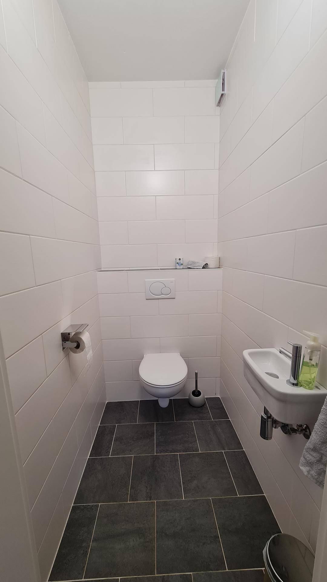 Kleines Gäste-WC mit Wand-WC, Waschbecken und dunklen Bodenfliesen.