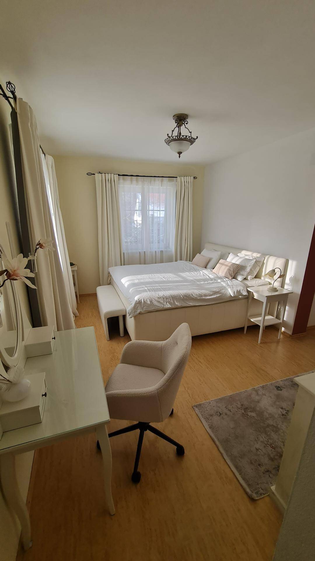 Helles Schlafzimmer mit Holzboden, großem Bett und Schreibtischbereich.