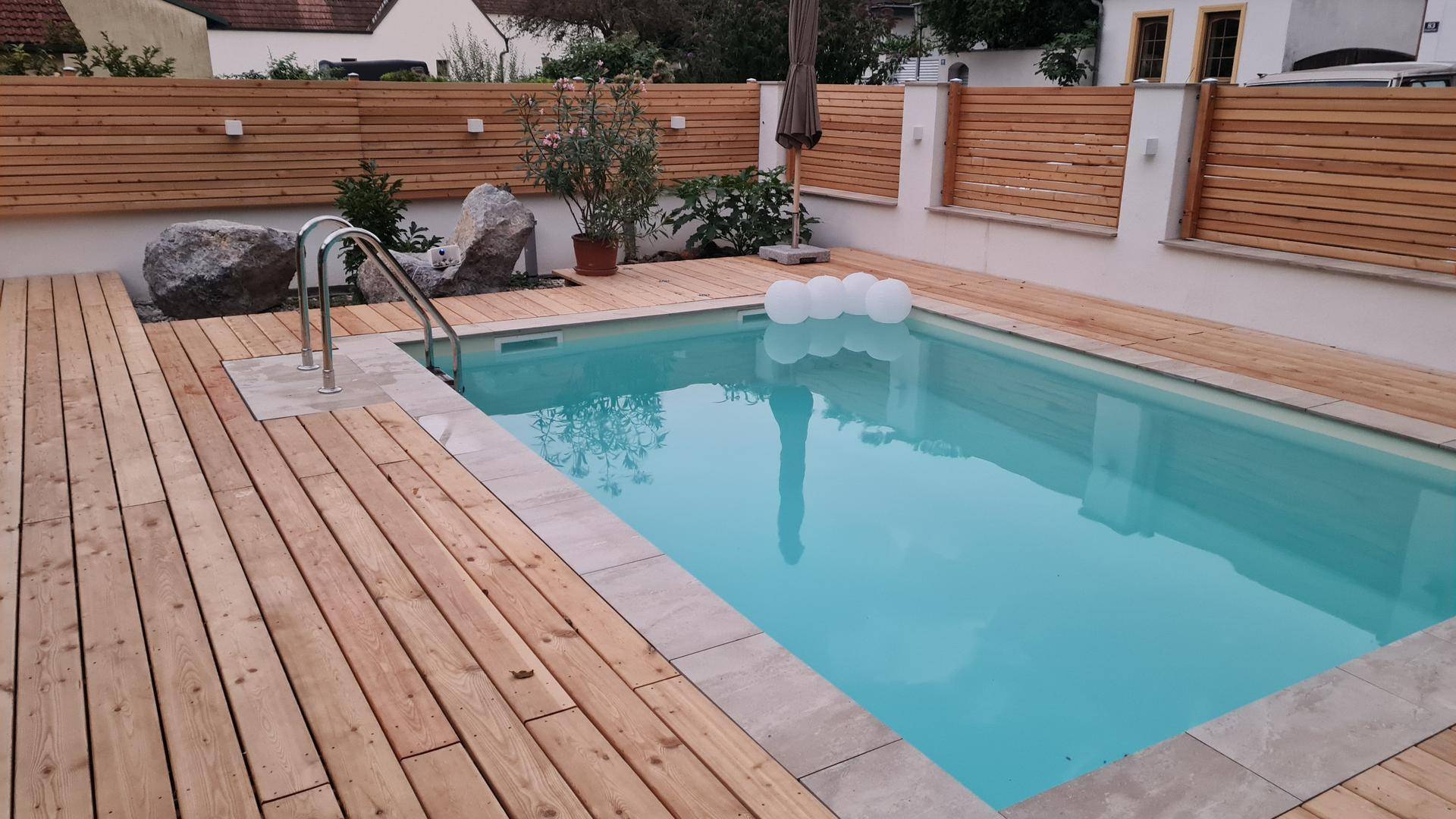 Außenpool mit Holzdeck und Steinumrandung, umgeben von einer Holzwand.