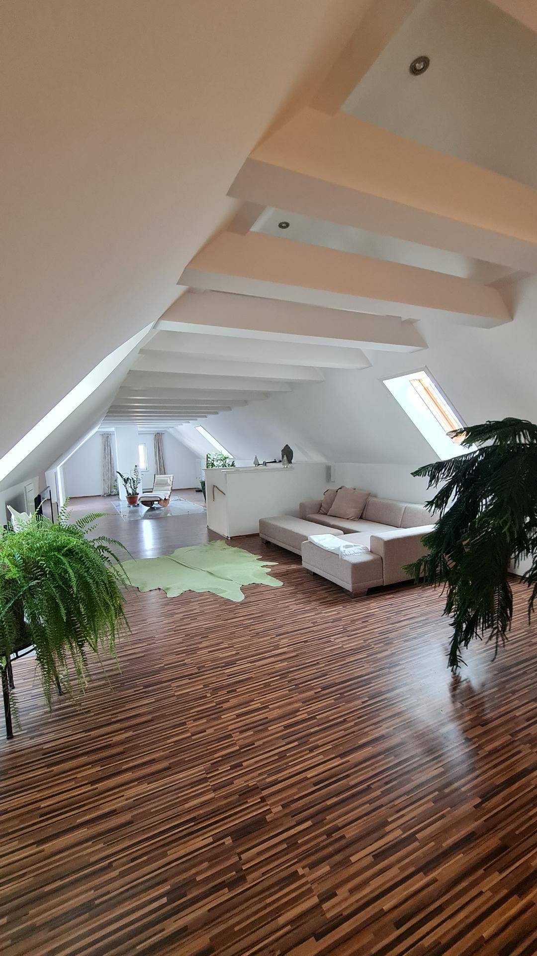 Helles Dachgeschoss-Wohnzimmer mit Holzboden, Dachschrägen und gemütlicher Sitzecke.