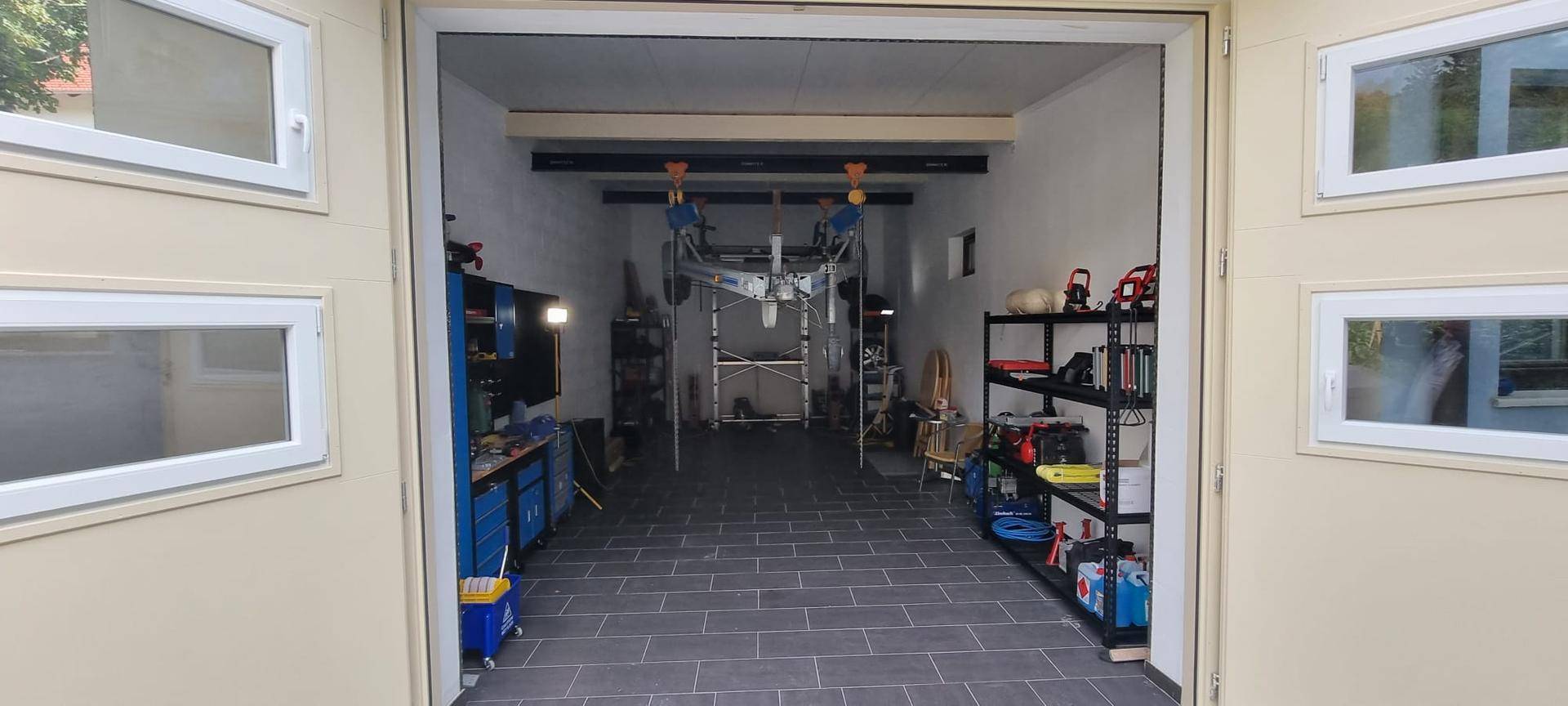 Geräumige Garage mit Werkbänken, Regalen und Fliesenboden.